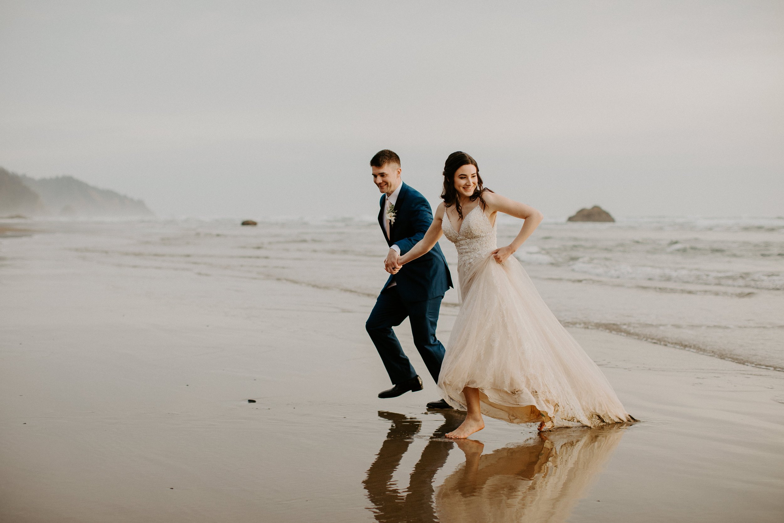 Bride and groom running away from the waves at the Oregon coast