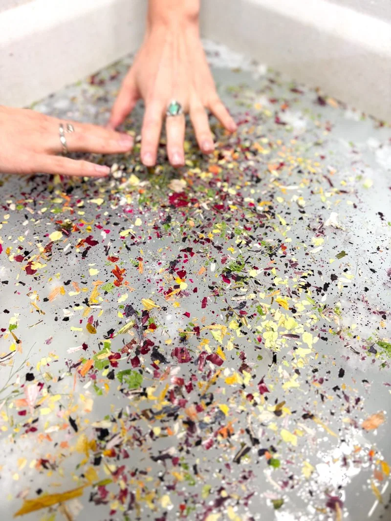 White woman's hands in a papermaking vat full of flower petals