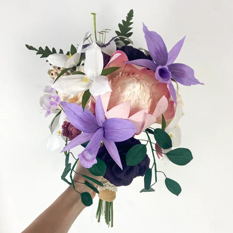 Handmade paper flower bouquet with purple orchids, pink blooms, white flowers, and green foliage