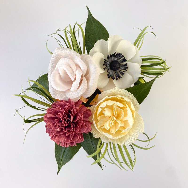 Handmade paper flower arrangement with blush, cream, yellow, and burgundy blooms surrounded by green foliage