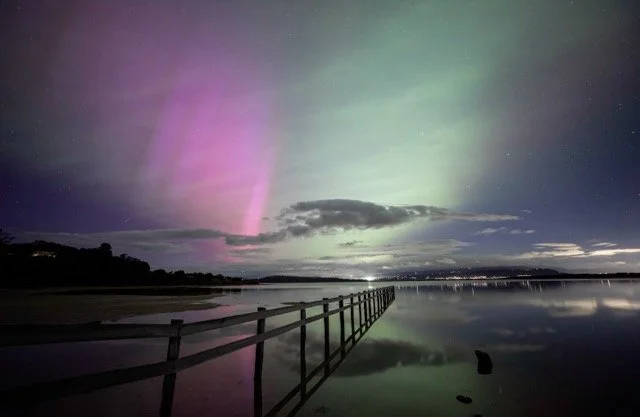	
Southern lights over a lake with a wooden pier and cloudy sky.