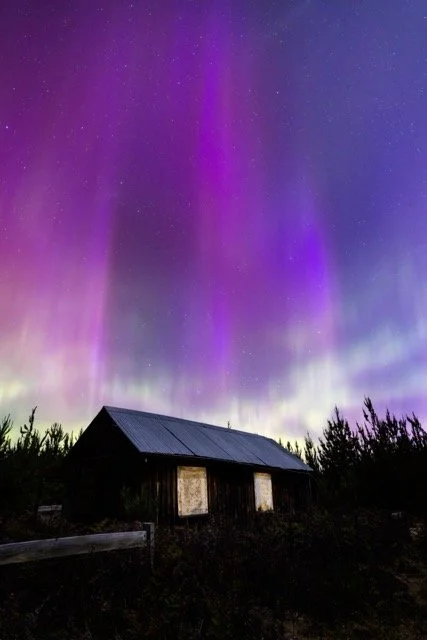 A house under a vibrant display of the Southern lights with purple, green, and blue hues in the night sky.