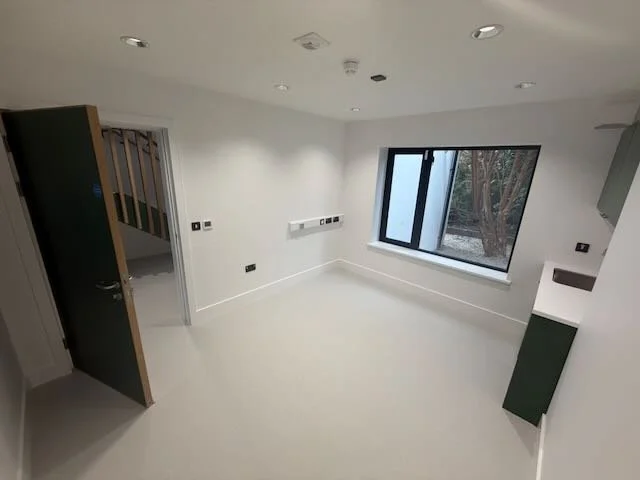 Empty room with white walls, a large window, a door slightly open, and built-in electrical outlets.