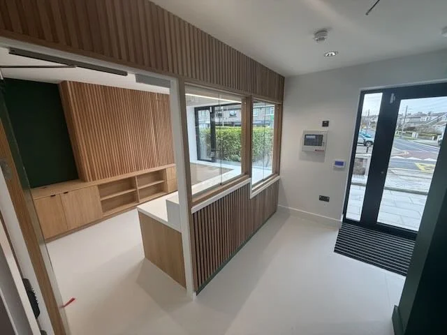 Empty modern reception area with wood paneling, a window, and a glass entrance door.