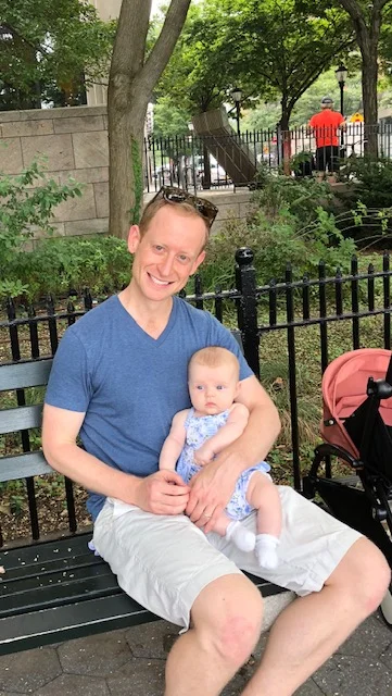 Alex and Maeve on a bench next to the Hudson River near the Statue of Liberty, August 2018