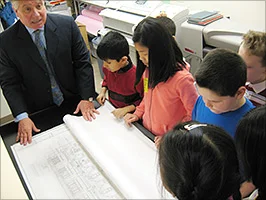 Michael Macaluso with Architots children in his office showing blueprints of a new building.