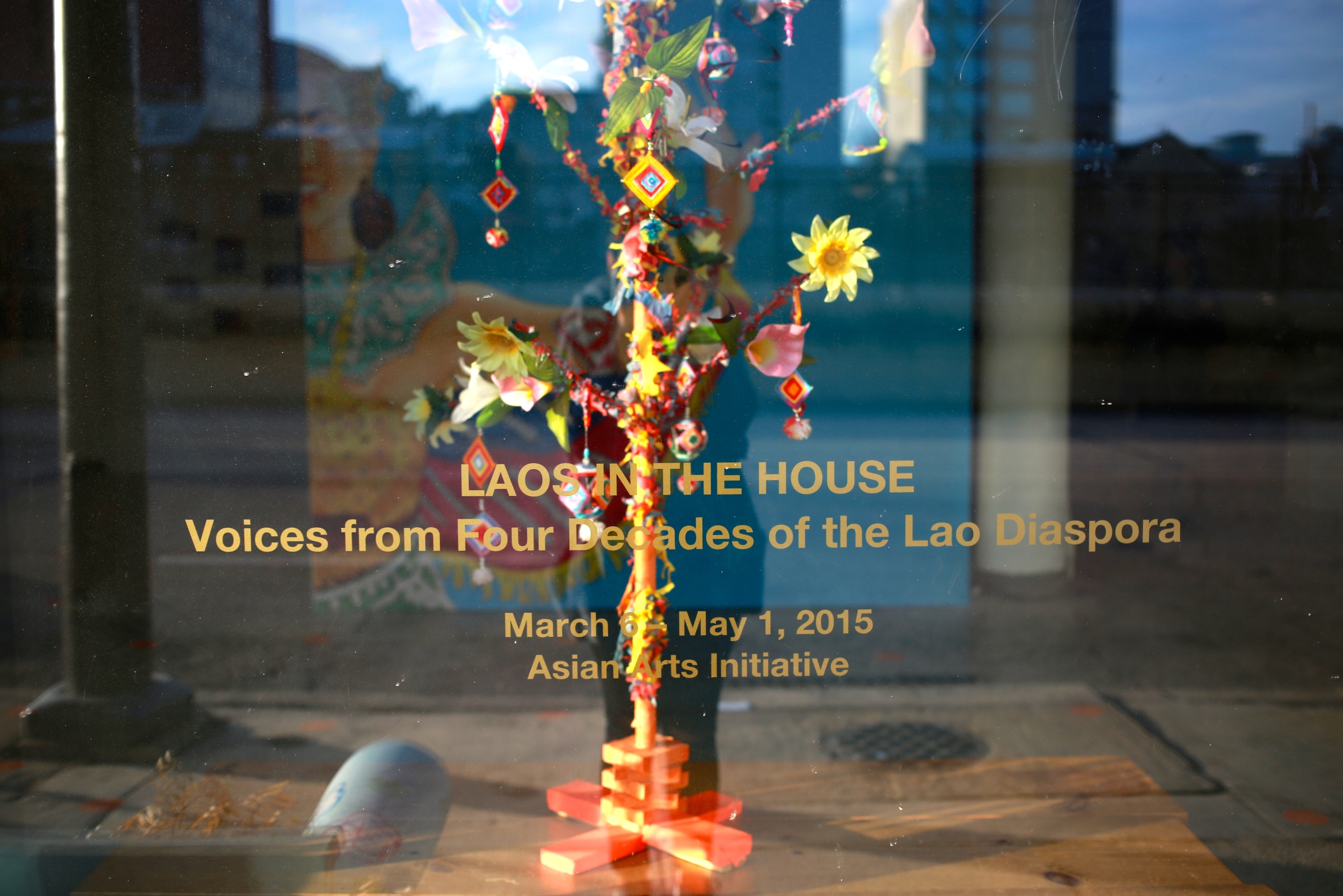 Front view of the Asian Arts Initiative gallery window with a "money tree” on loan courtesy of Wat Lao Phouthathammaram