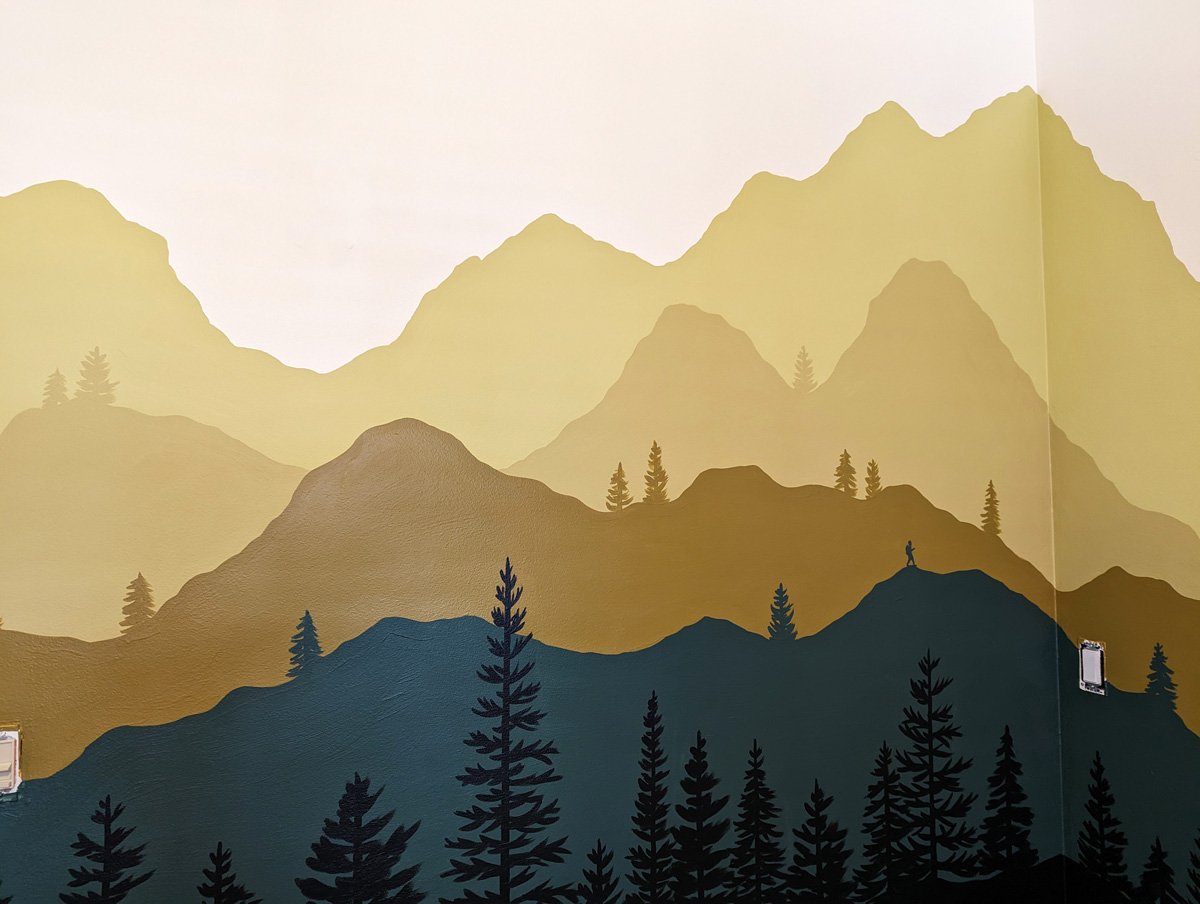 Mountain Bedroom mural painted in michigan with mountain layers and pine trees in green and gold.