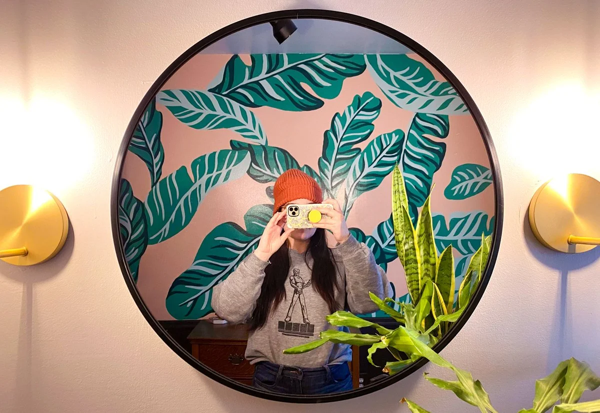 Tropical bathroom mural in Marquette Michigan with banana leaves on pink, mirror selfie