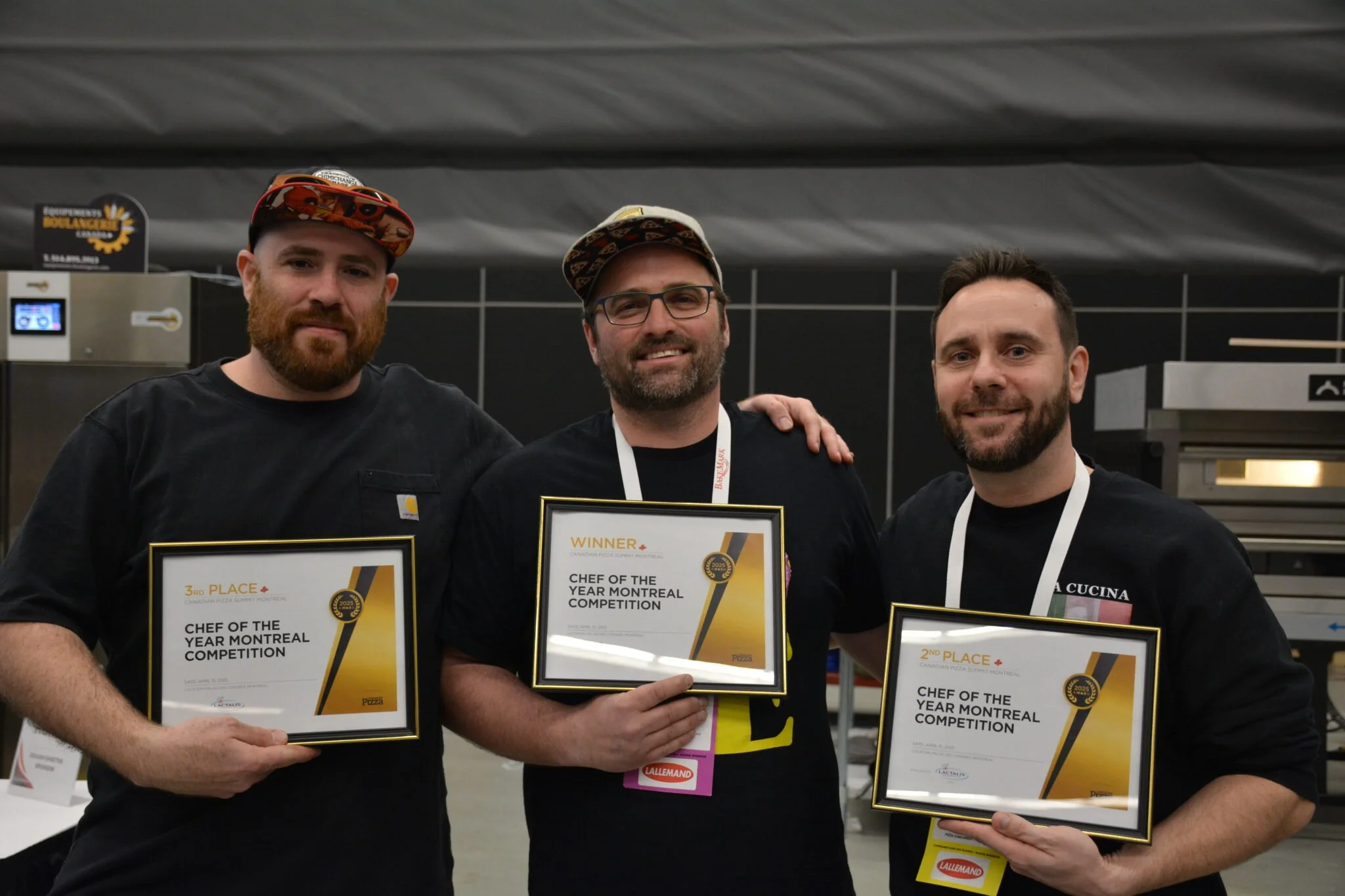 Three men holding certificates of achievement in a cooking competition, smiling for the camera, in a kitchen setting.