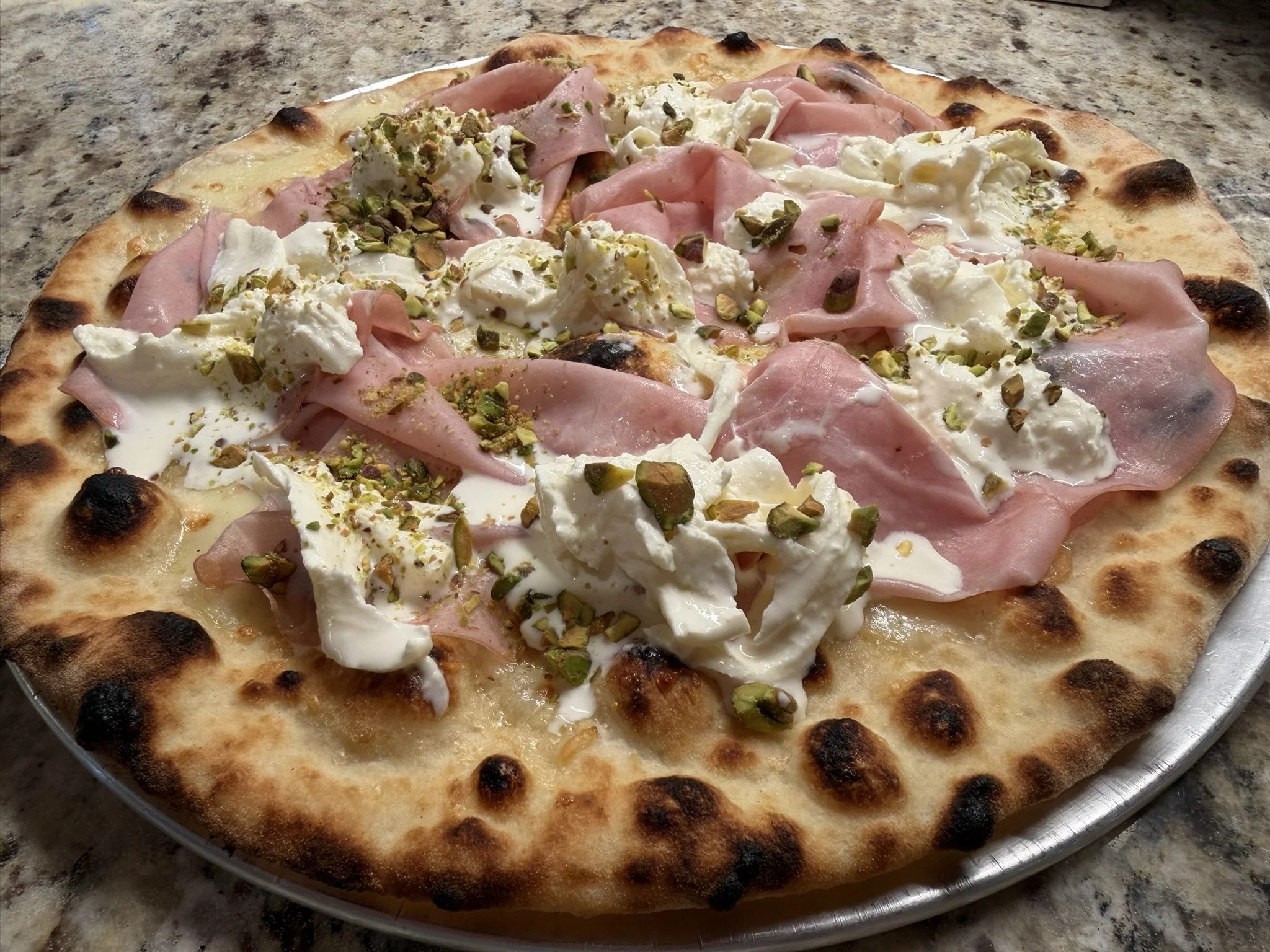 A pizza with a thin crust, topped with slices of Mortadella, Stracciatella cheese, and chopped pistachios.