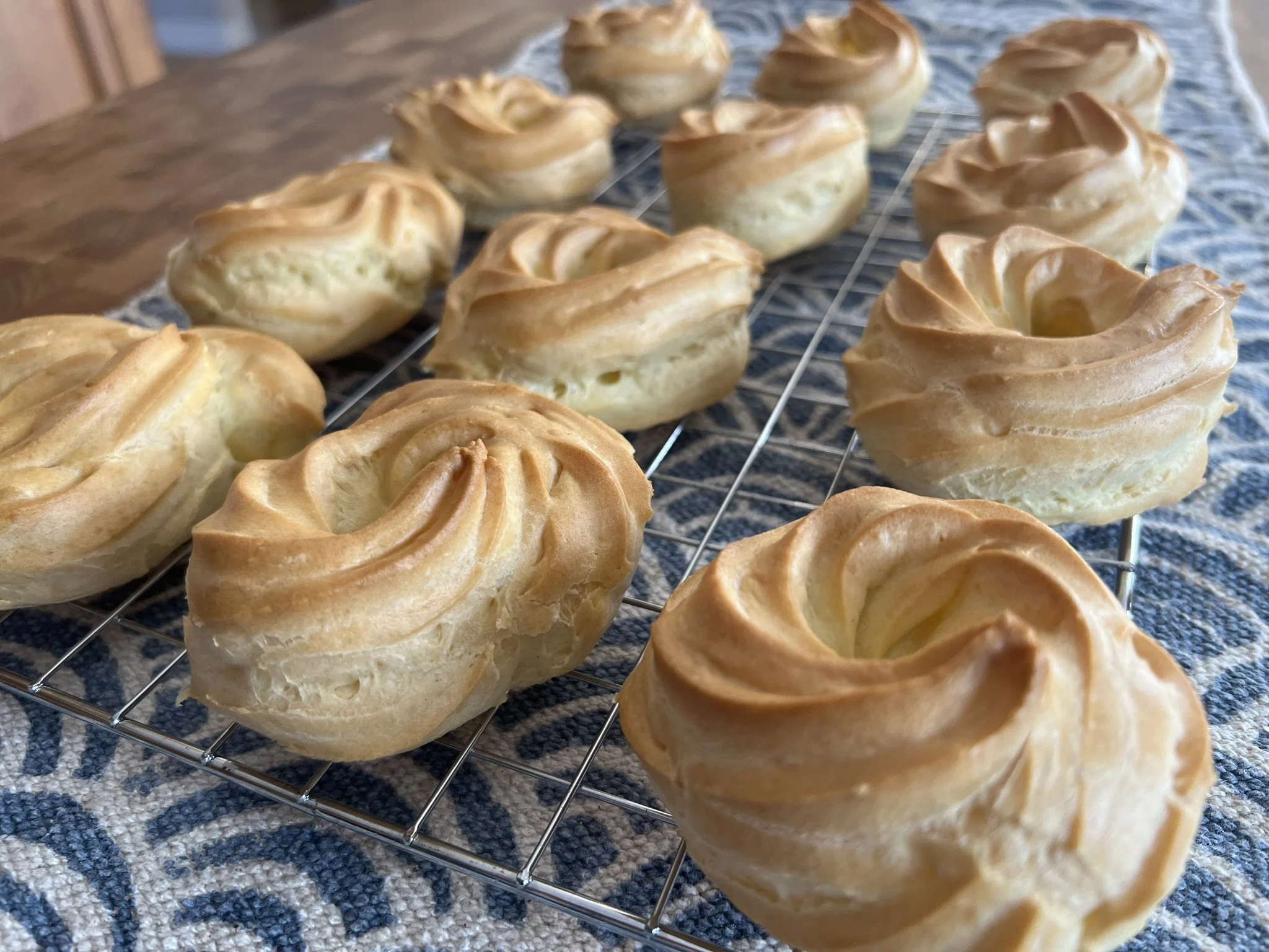 Freshly baked Zeppole cooling on a wire rack on a patterned tablecloth.