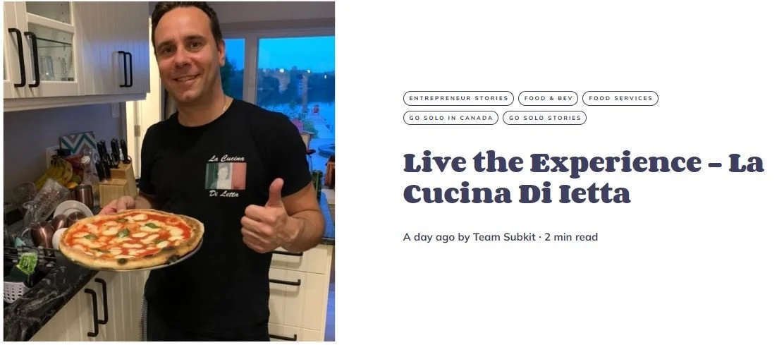 A man in a kitchen holding a pizza and giving a thumbs up.