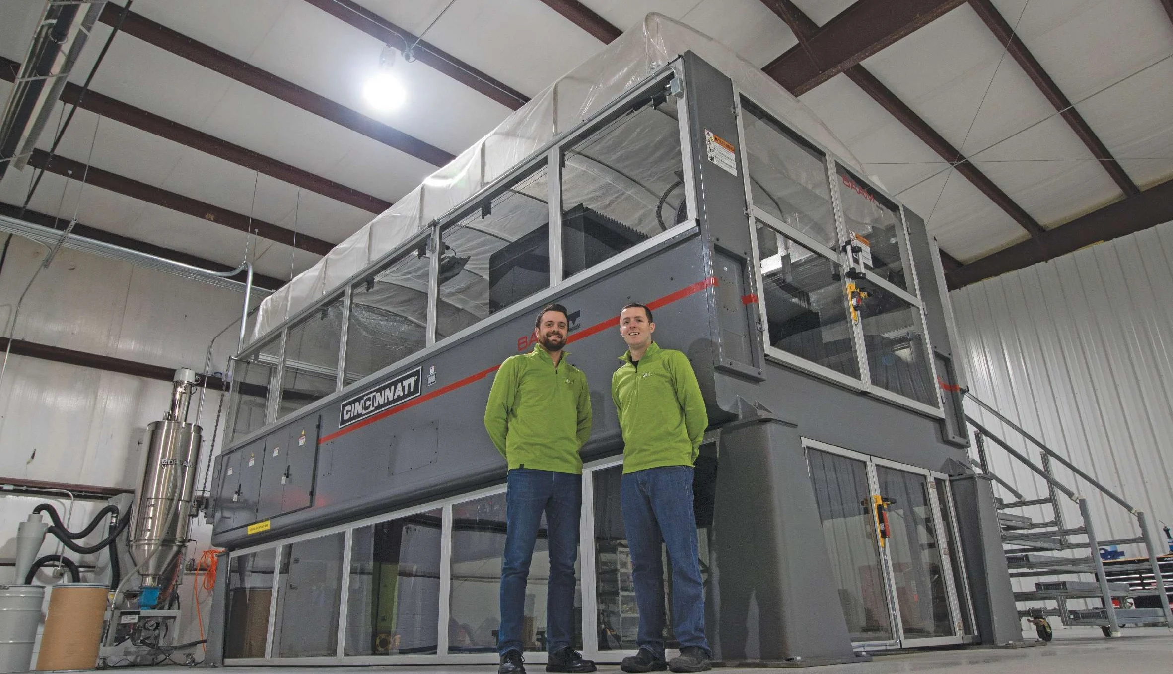 Andrew Bader and Austin Schmidt stand in front of the Big Area Additive Manufacturing machine that is the basis for their business.