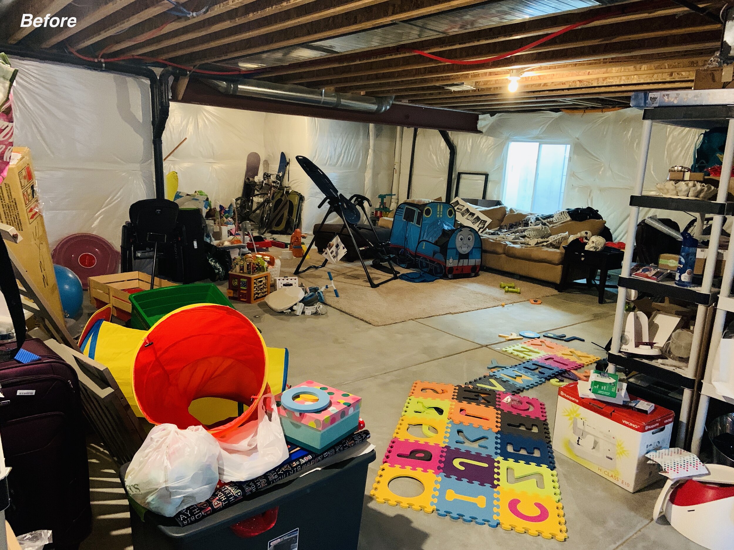Large unfinished basement before photo with toys and items covering floor.