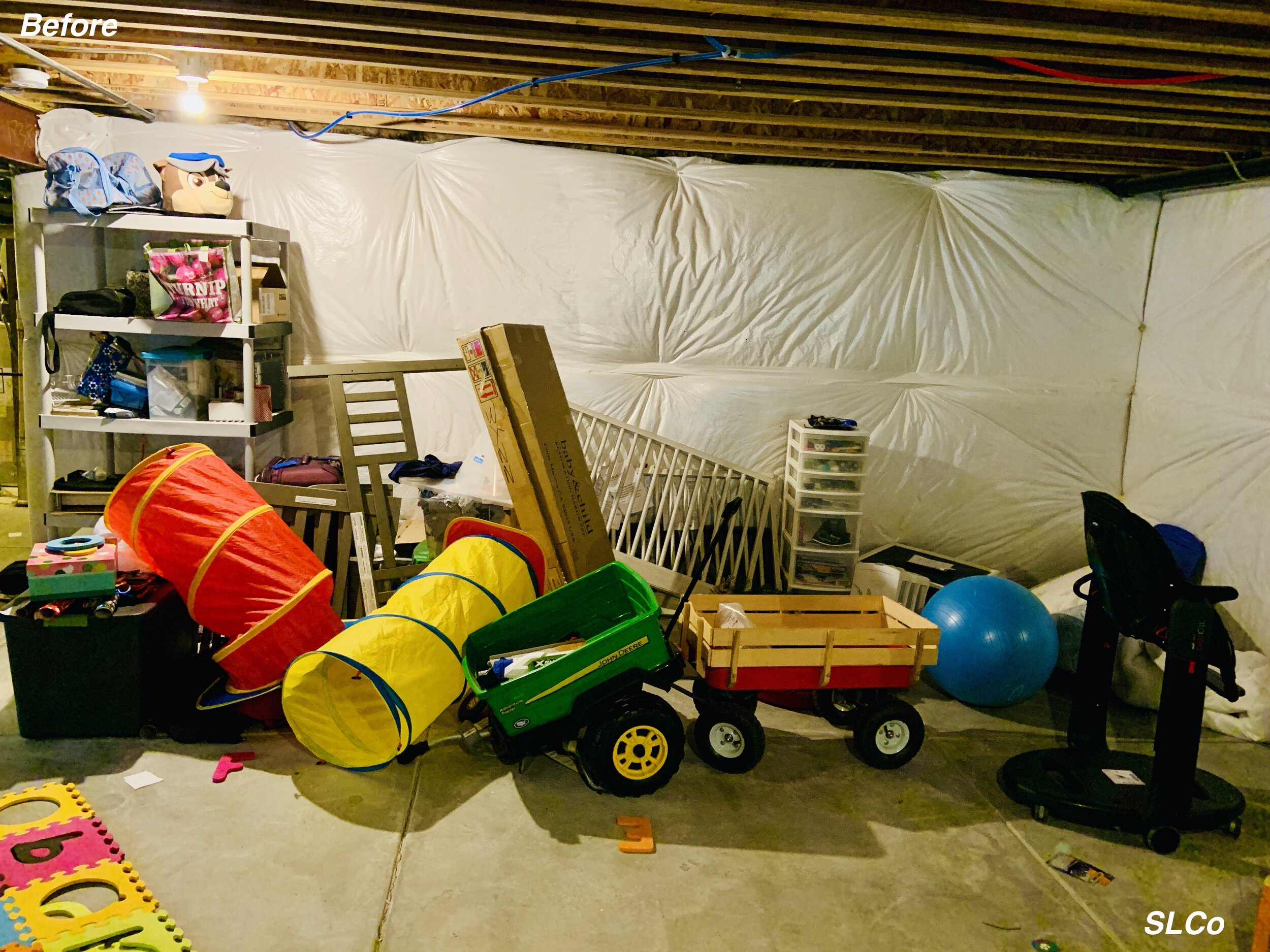 Before photo of unfinished basement with toys and a shelf covering floor