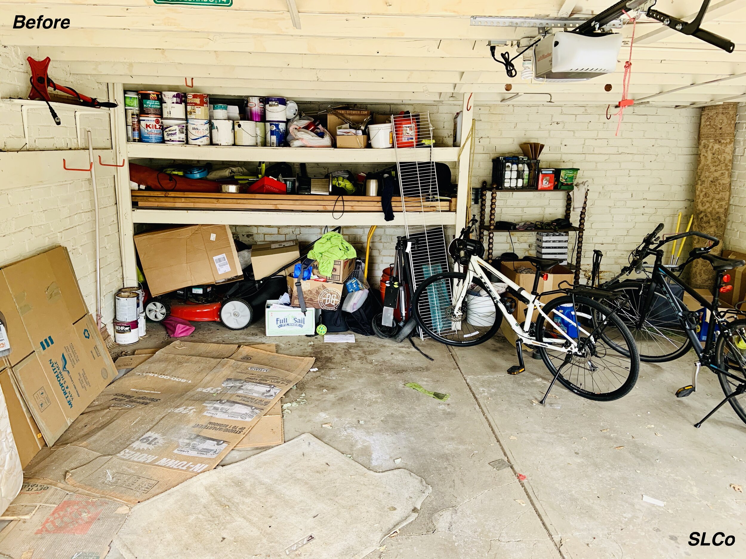 Before photo of garage with built in long shelves filled with paint cans, wood, and bottom with stacked random items
