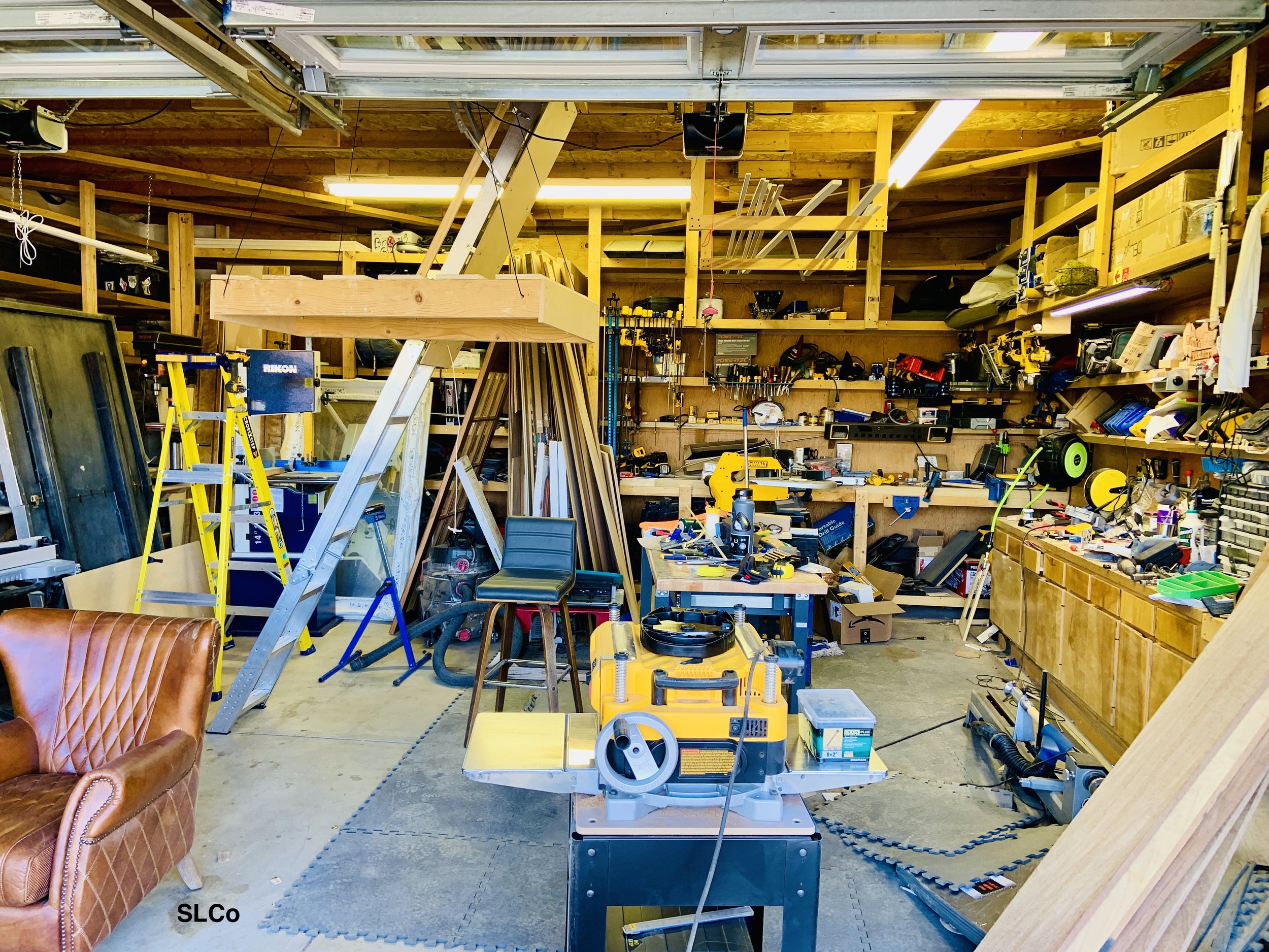 Workshop with wools and wooden shelves with all counters filled with tools and items and table in the front also covered.