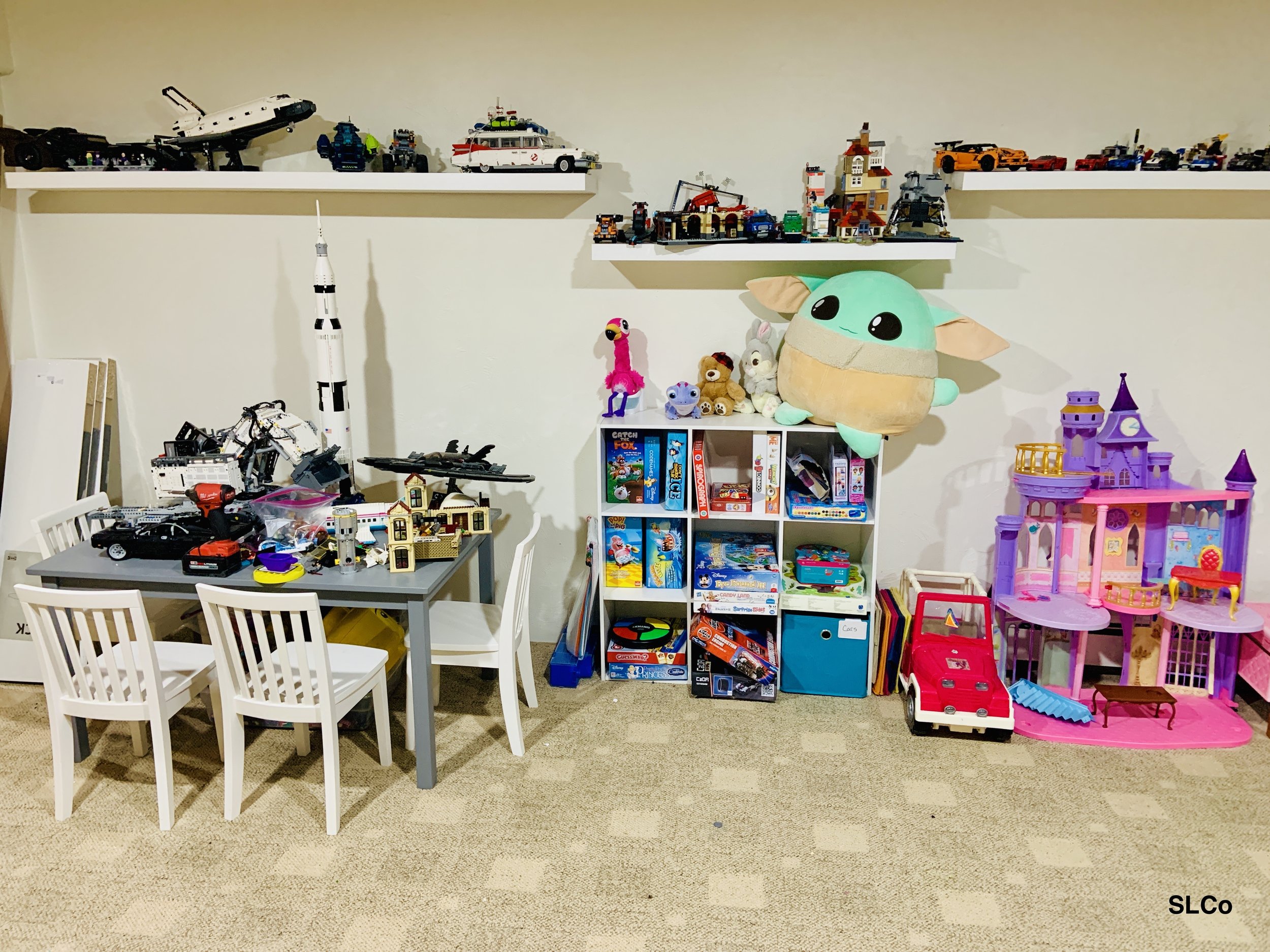 After photo of playroom wall with smaller desk and shelves with lego displayed and toys organized.