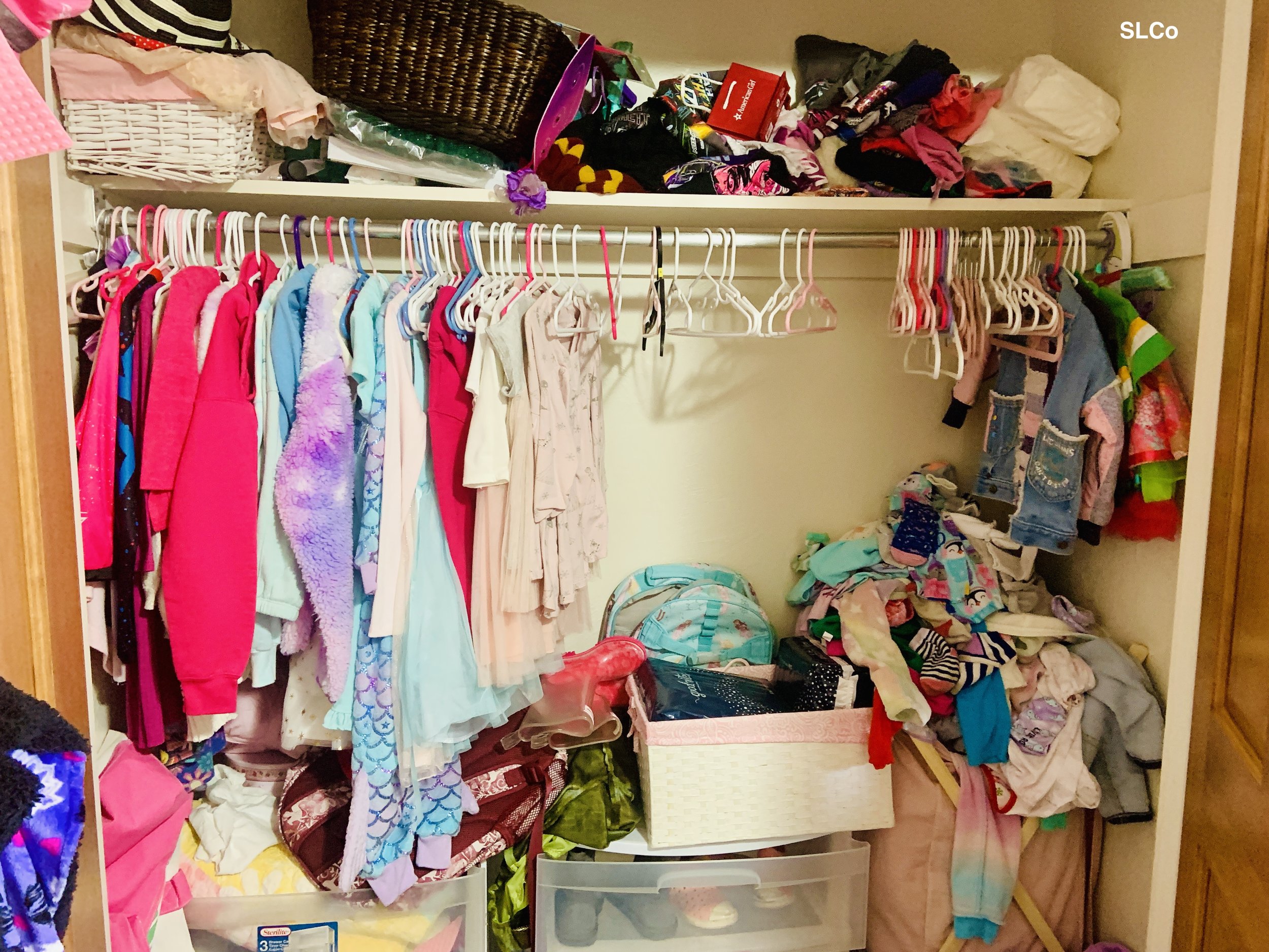 Little girls closet with containers and clothes stacked on the floor and hanging clothes and hangers in dissaray