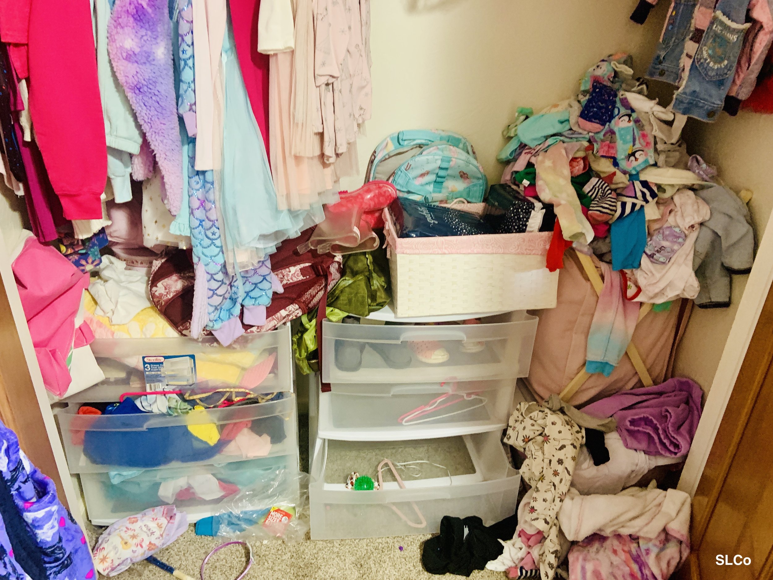 Bottom of little girls closet with white and clear drawered three bin storage containers with hangers and clothes thrown in them.