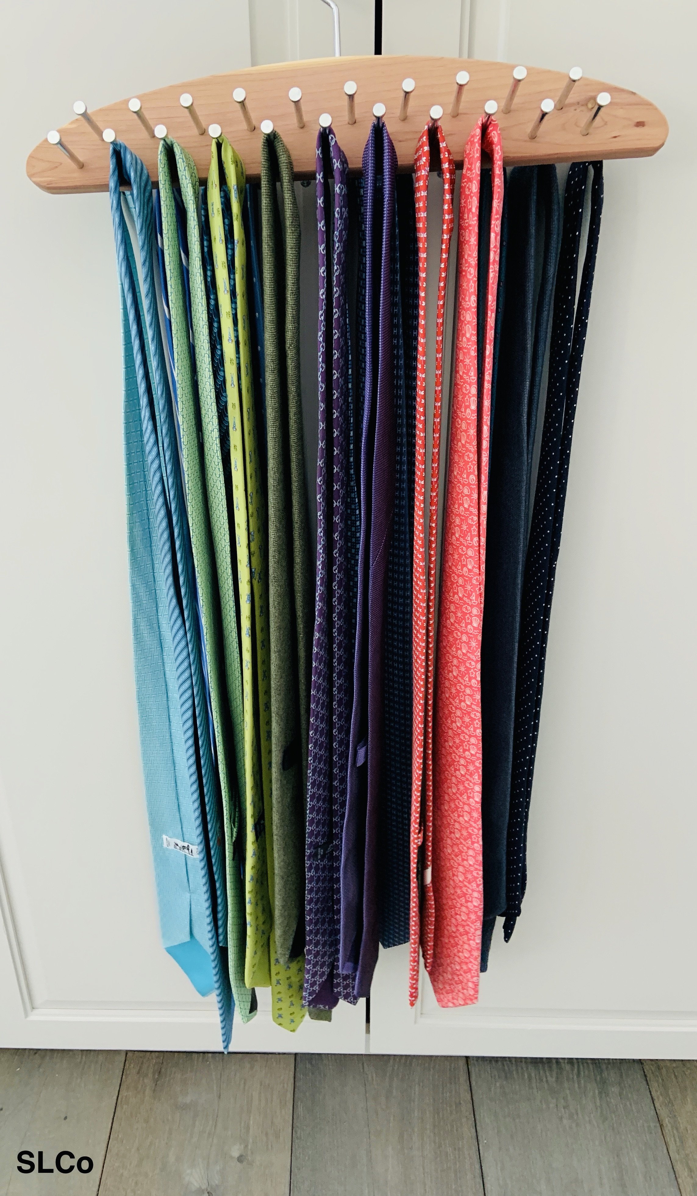 Ties organized and hanging on a wooden hanger with a silver nail like spot for each tie.