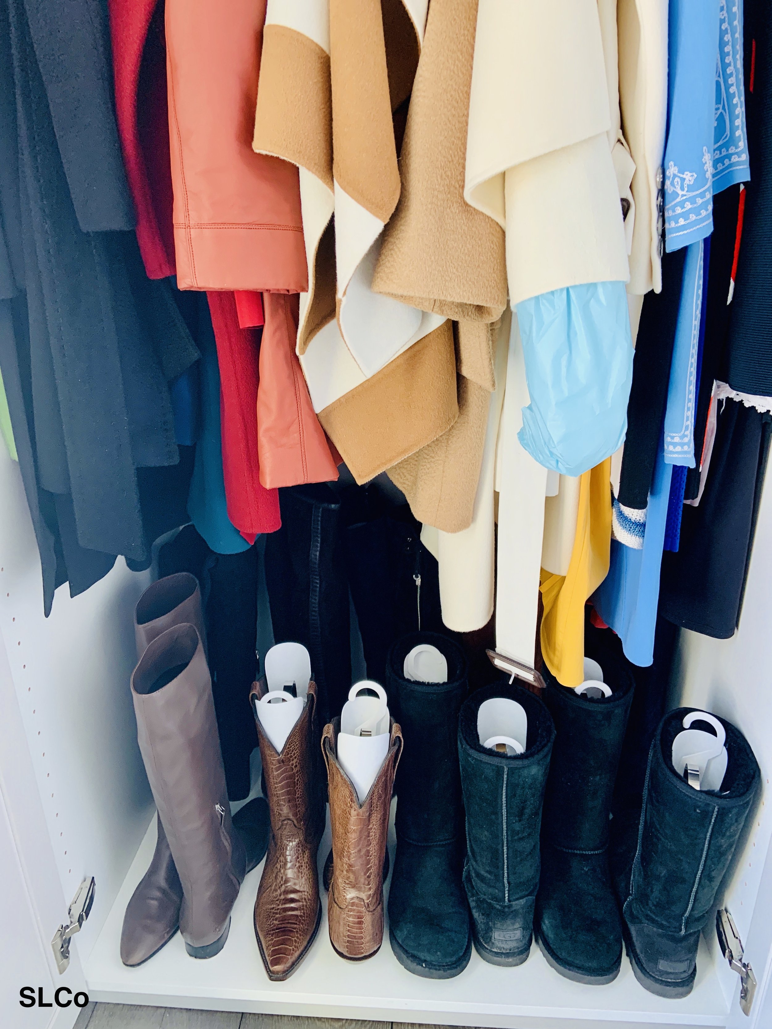 Clothes hanging in a small closet and tall boots on the bottom.