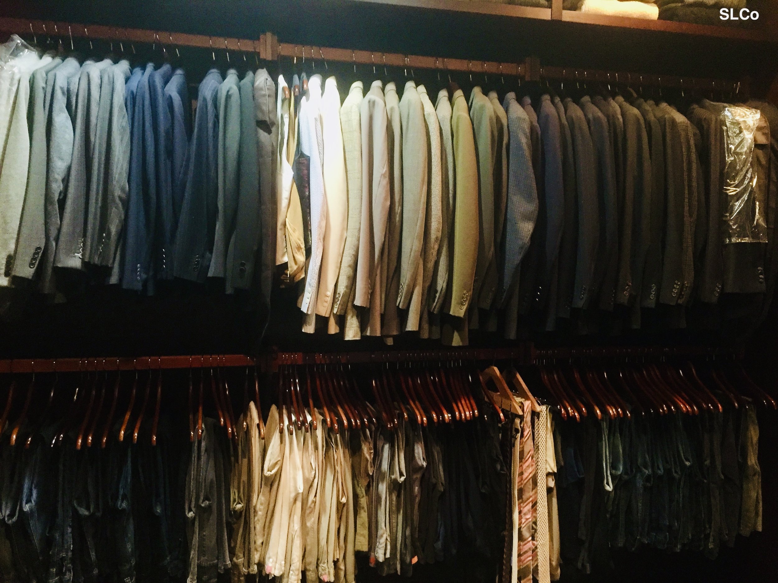 Large mens closet organized with shirts hanging with all same colors together on two rows of hanging dress shirts on bars