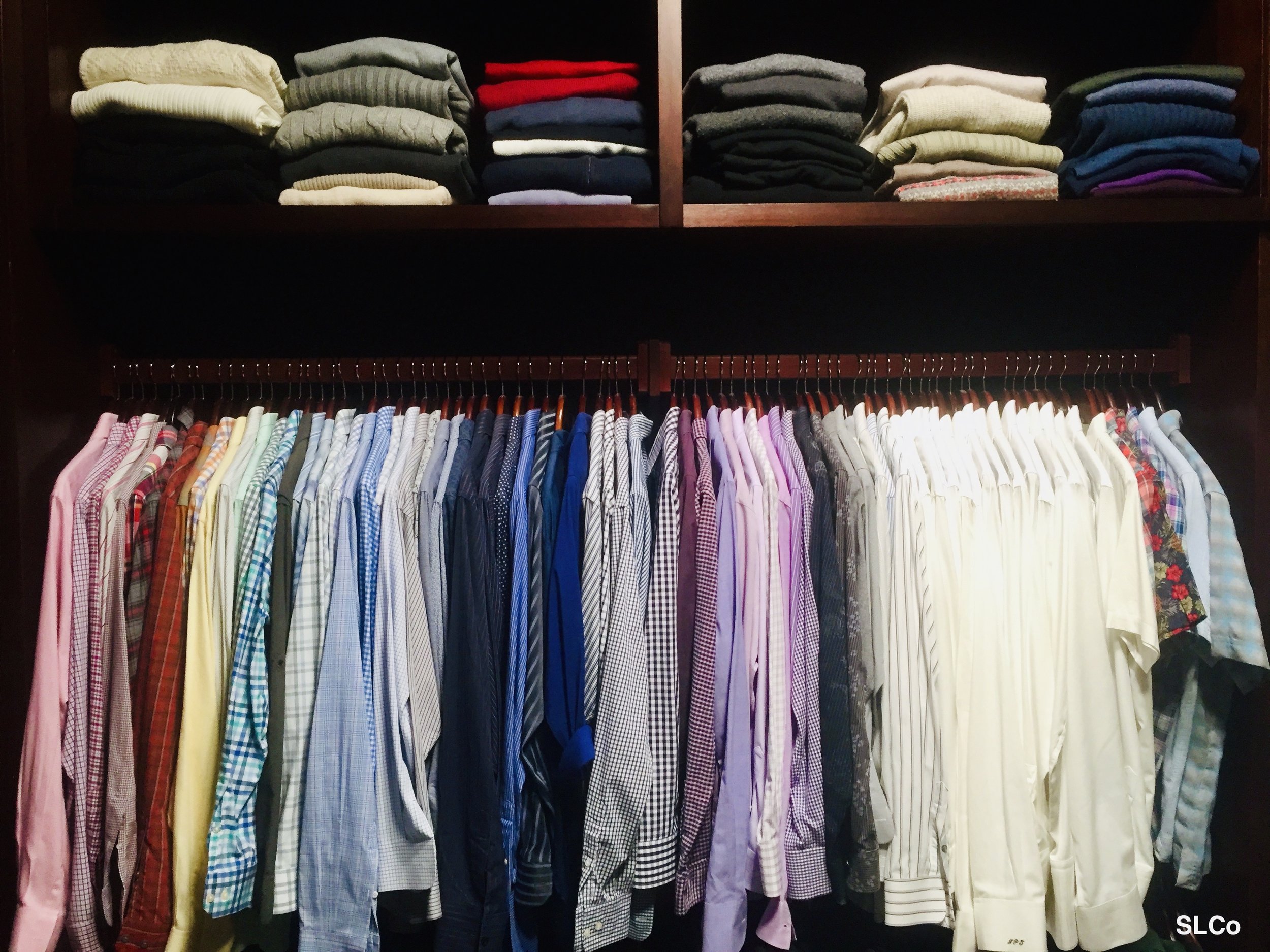 Mens closet with wooden shelves above hanging items, with folded dress shirts
