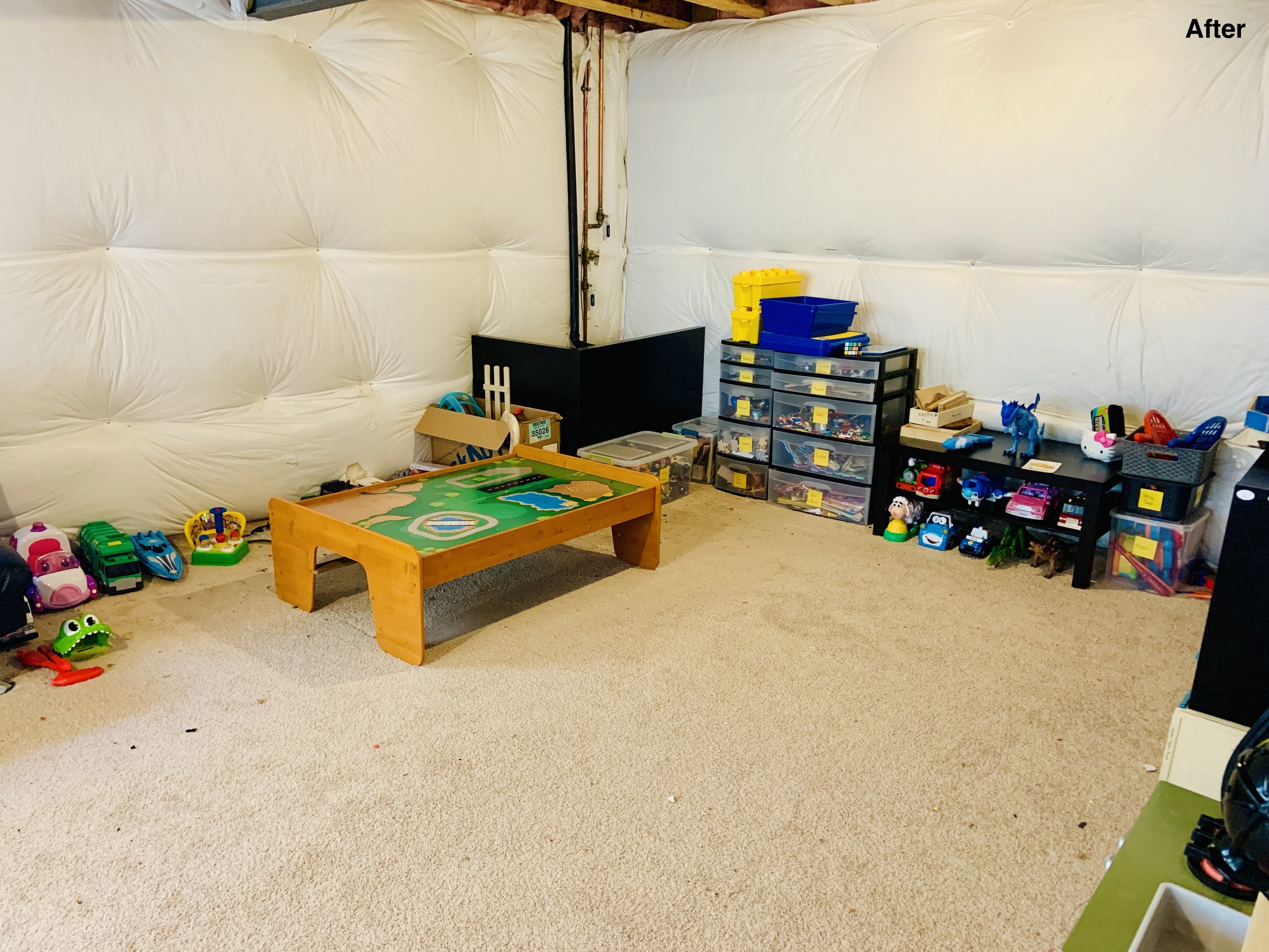 After photo of playroom with carpeted floor and toys around the edges in labeled containers and shelving units.