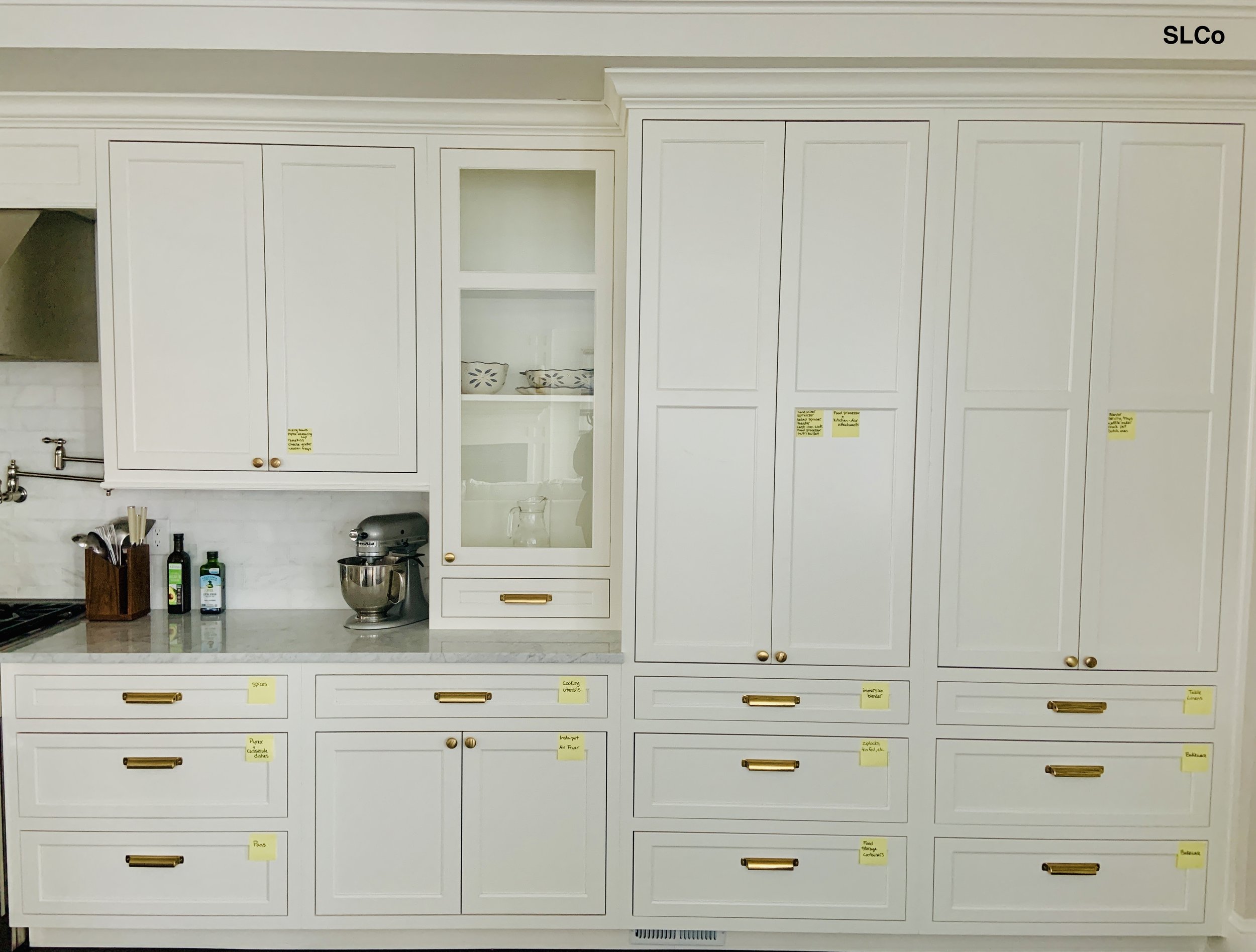 Larger overview photo of kitchen with white cabinets and granite counter with yellow post-it notes on the corners of all cabinets and drawers for labeling.