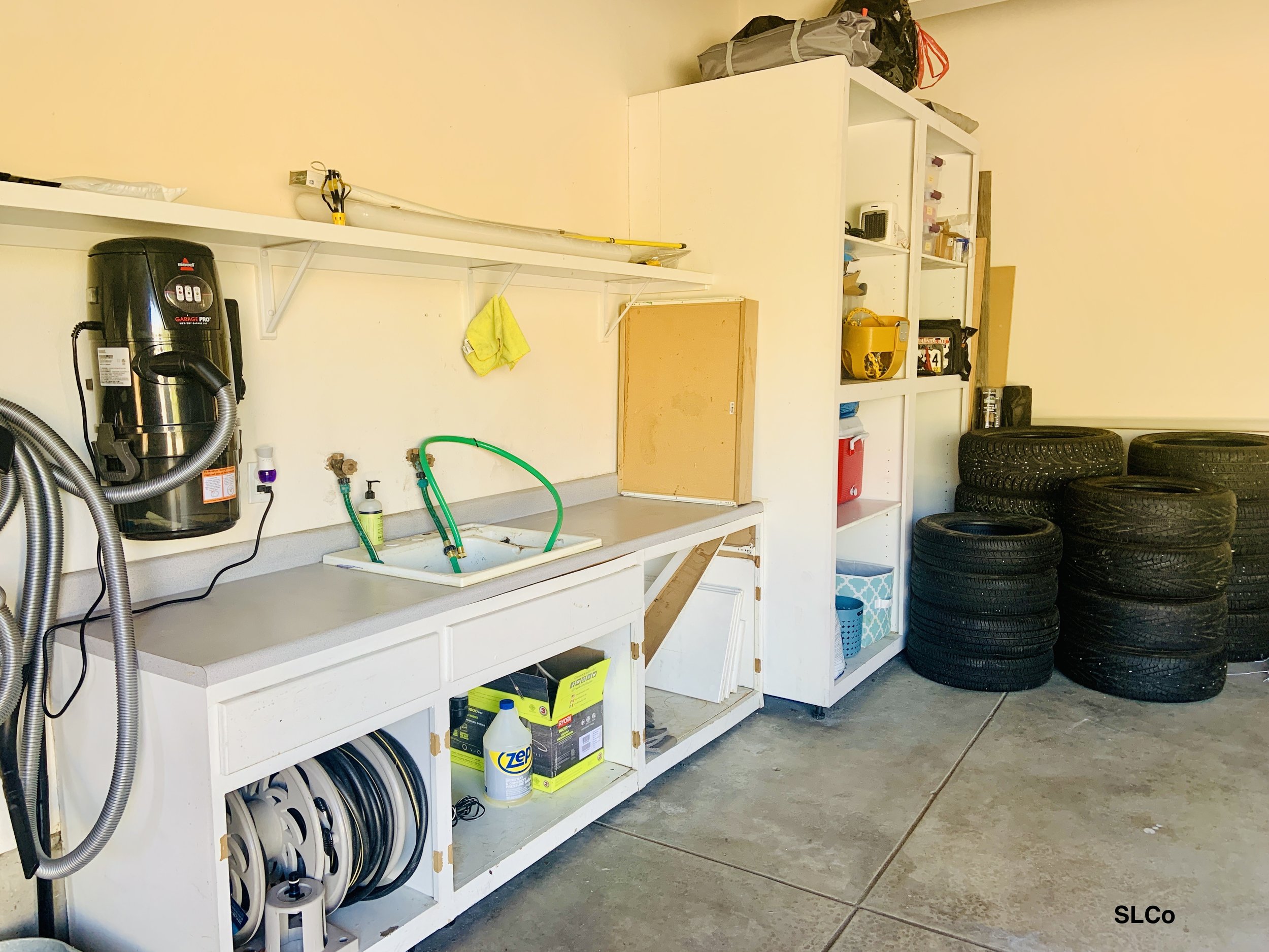 Garage with white built in large shelves and a counter and sink with counter and floor cleared and usable sink