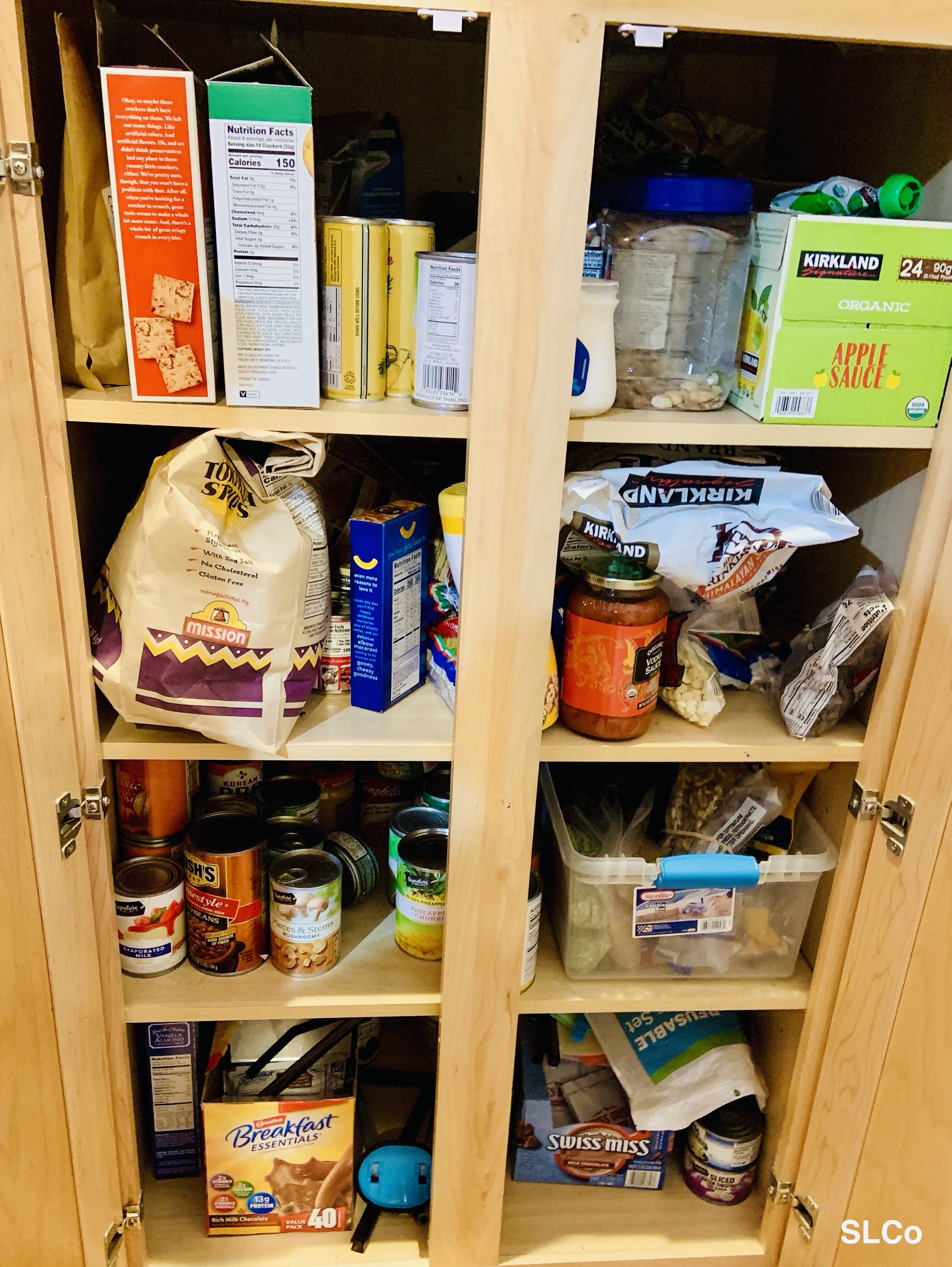 Kitchen cabinet 4 shelves high overflowing with cereal, chips, and cans
