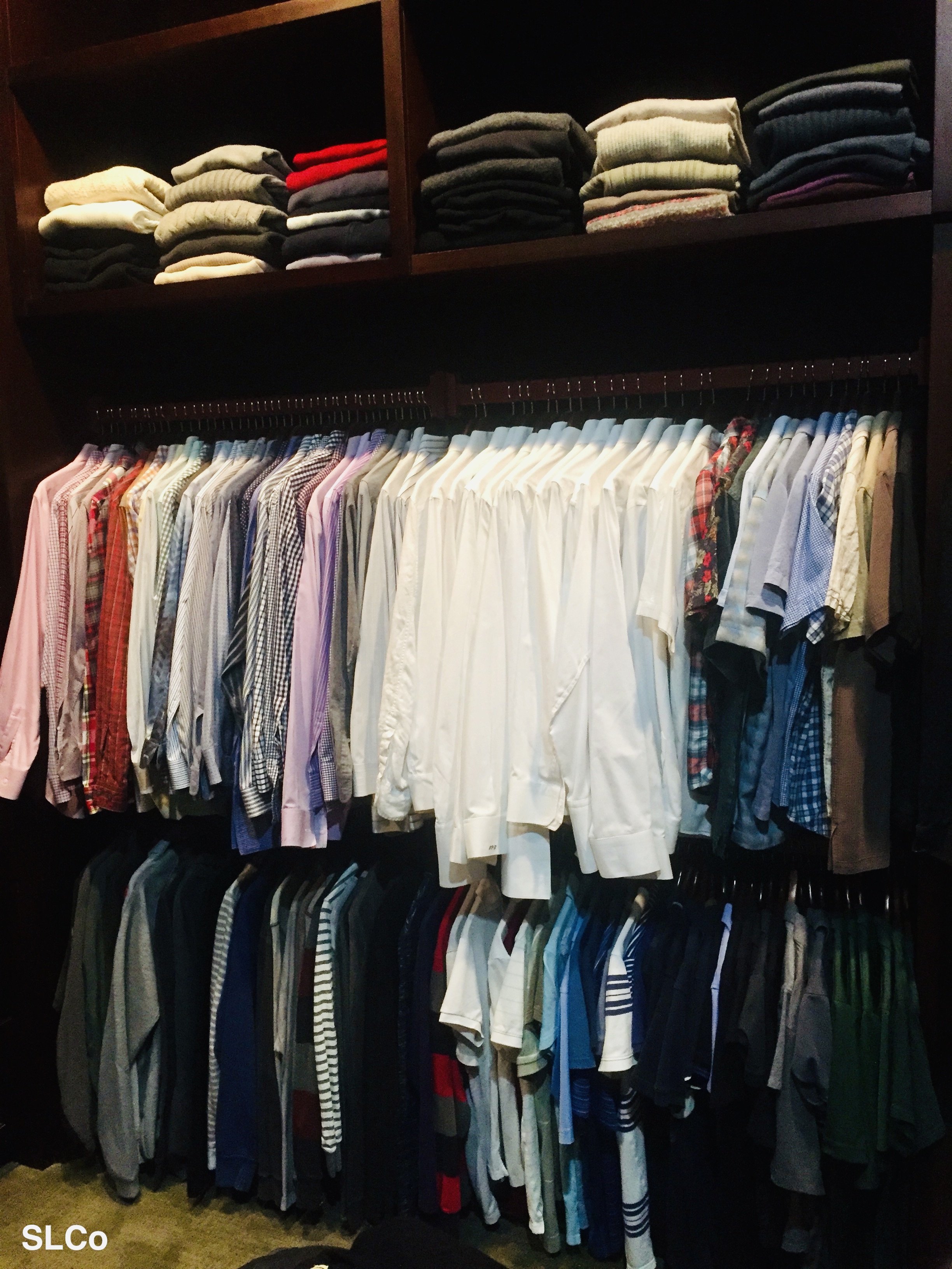 Two rows of dress shirts hanging and folded dress shirts on wooden shelves above