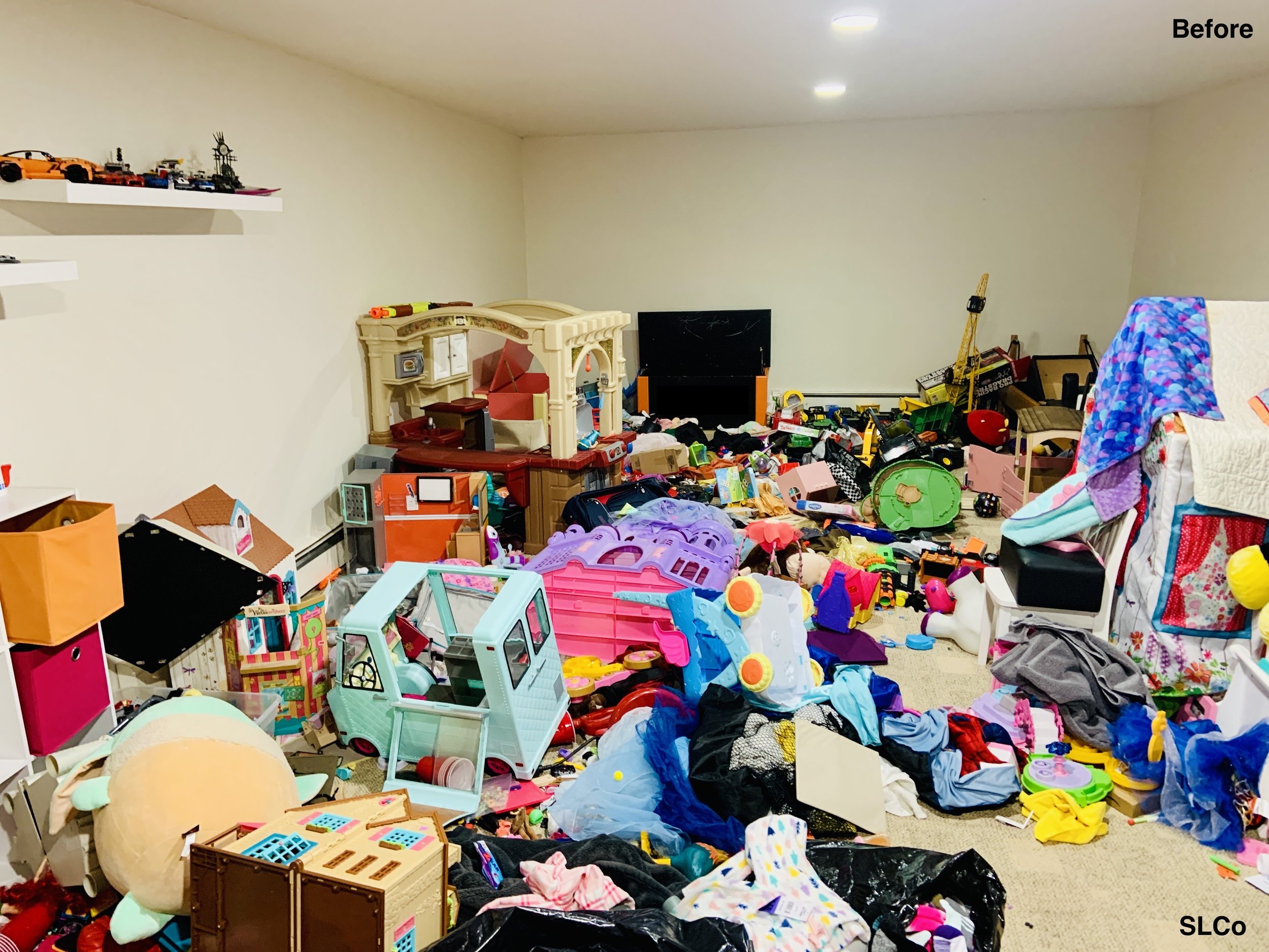 Before photo of playroom with trash bags with clothes on the floor, toys everywhere, and unwalkable.