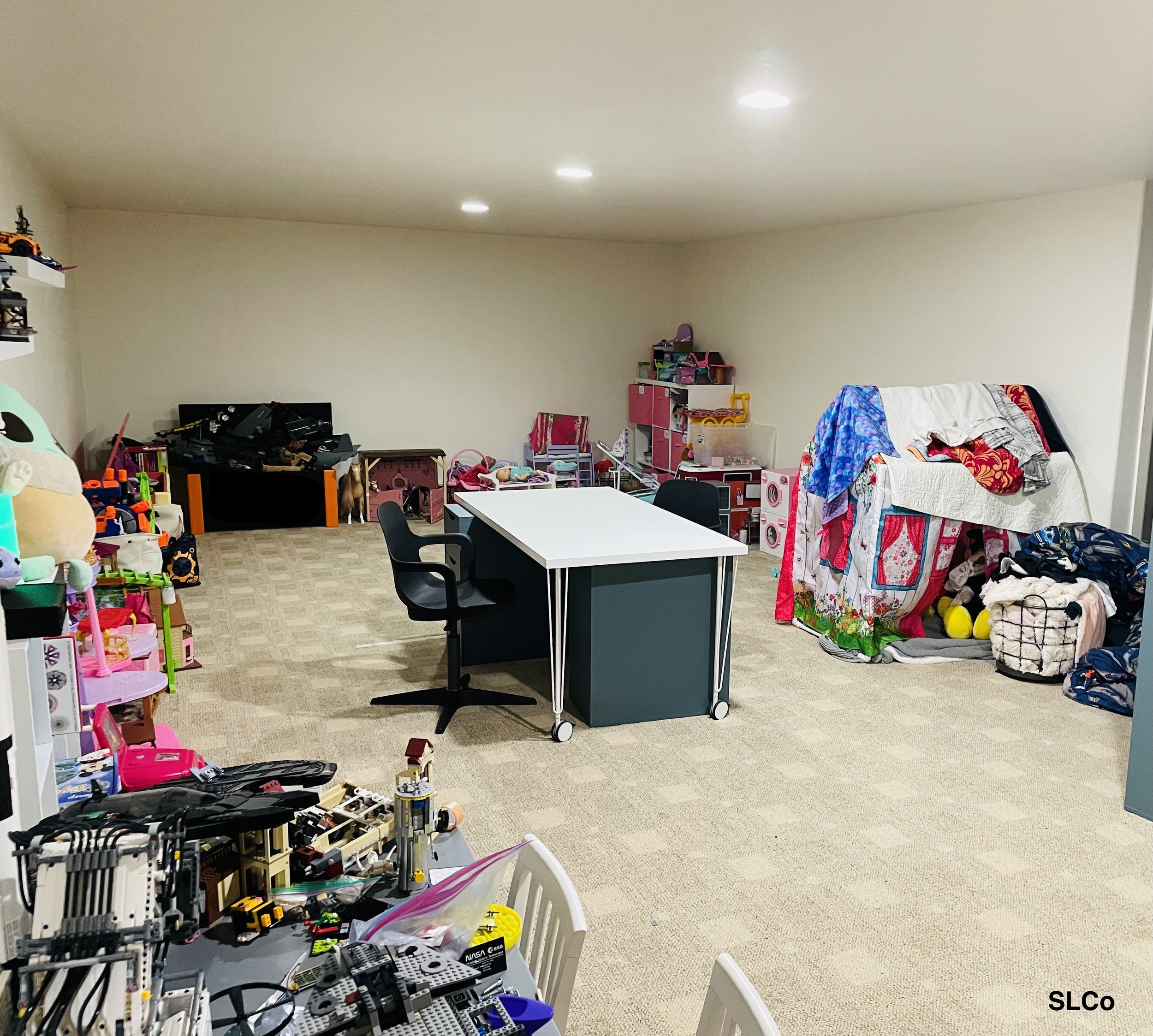 After photo of playroom with a clean desk in the middle of the room, clothes and toys around the walls organized on shelves.