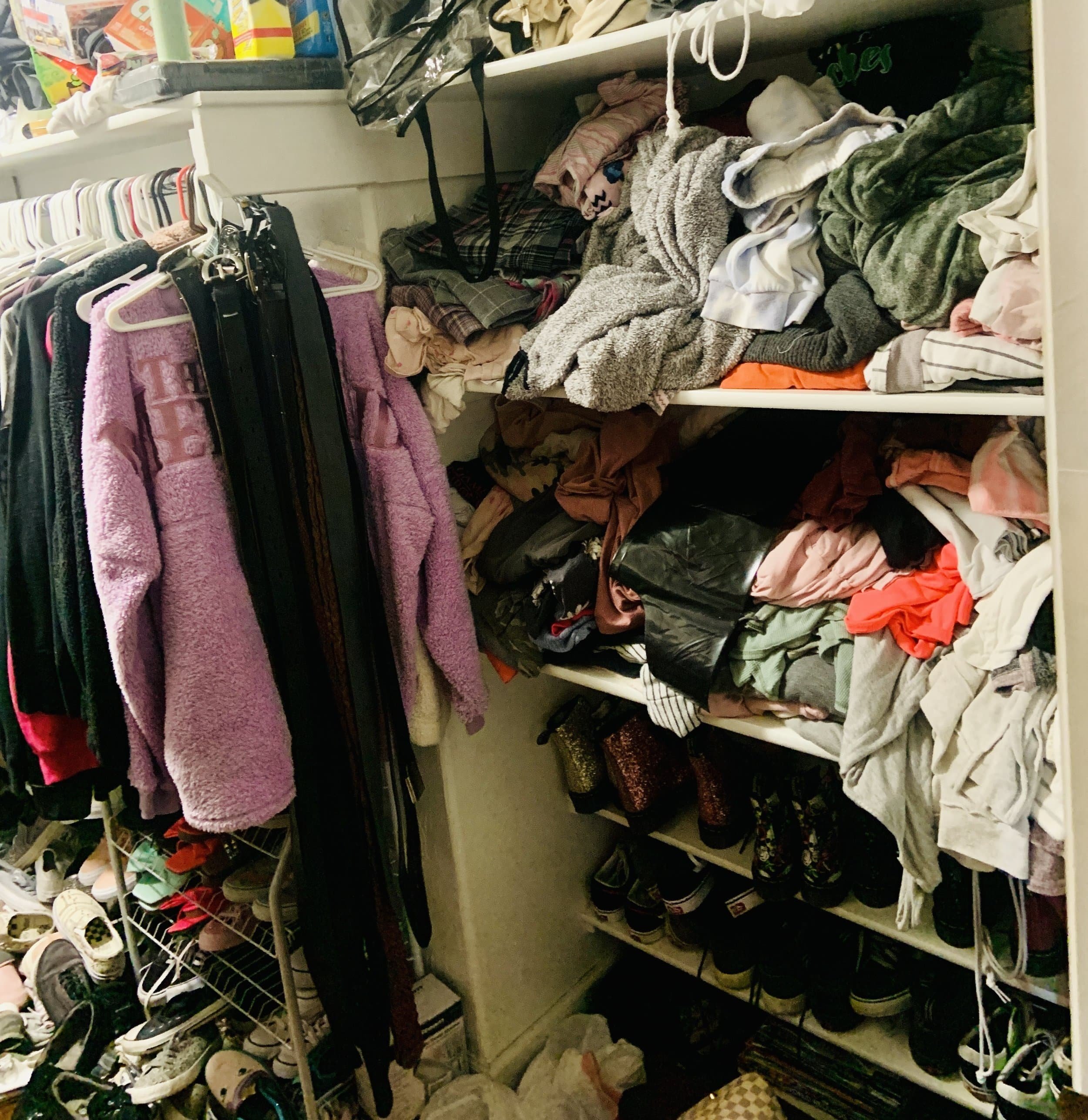 Walk in closet with horizontal shelved in the back with clothes thrown onto shelves and overflowing