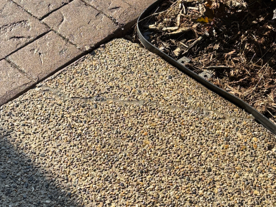 Close-up of a poured concrete sidewalk and brick paver sidewalk joint at the edge of a garden bed with mulch.