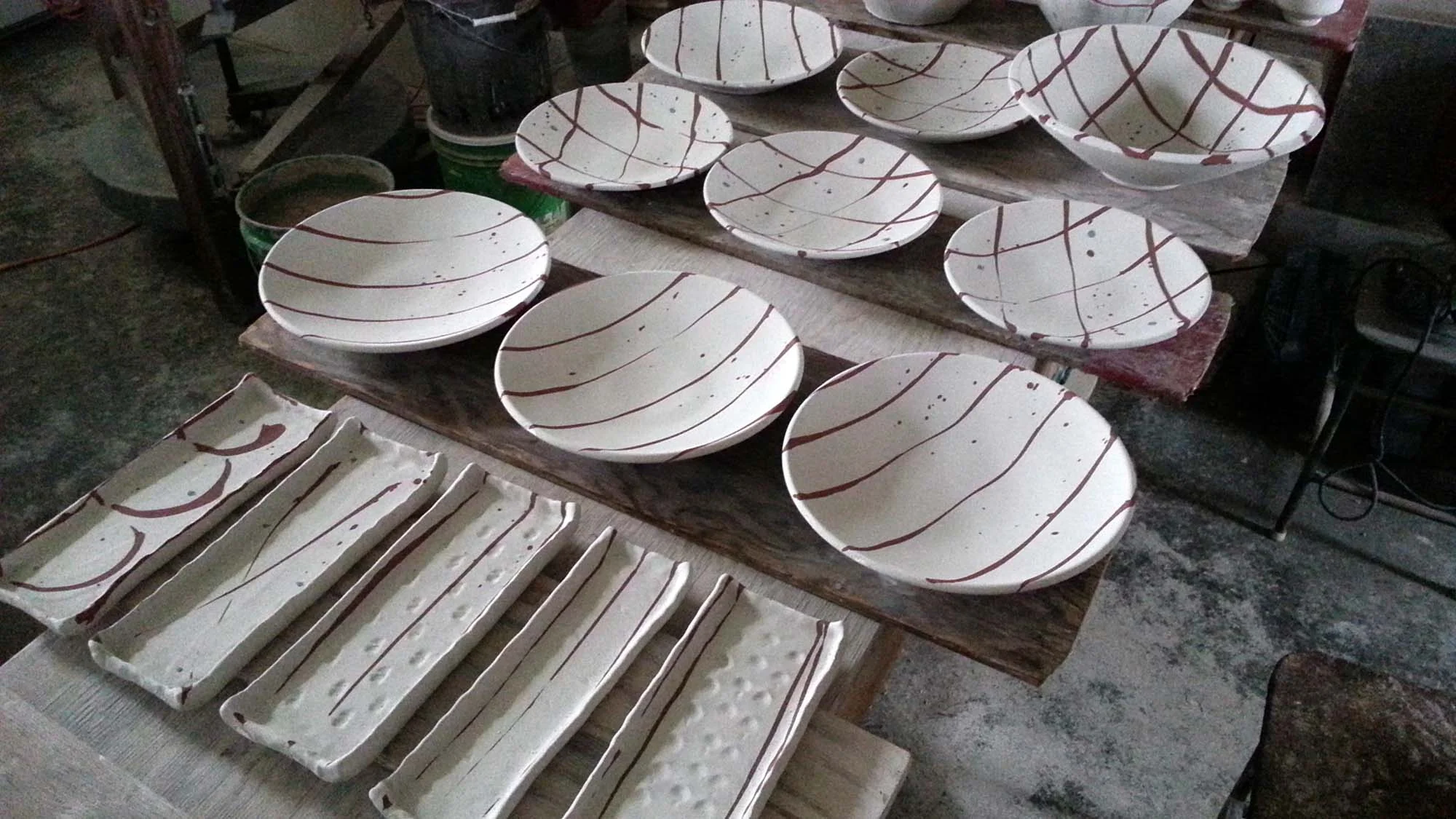 Plates and trays with raw glaze and iron oxide brush marks. Ready to be fired. 