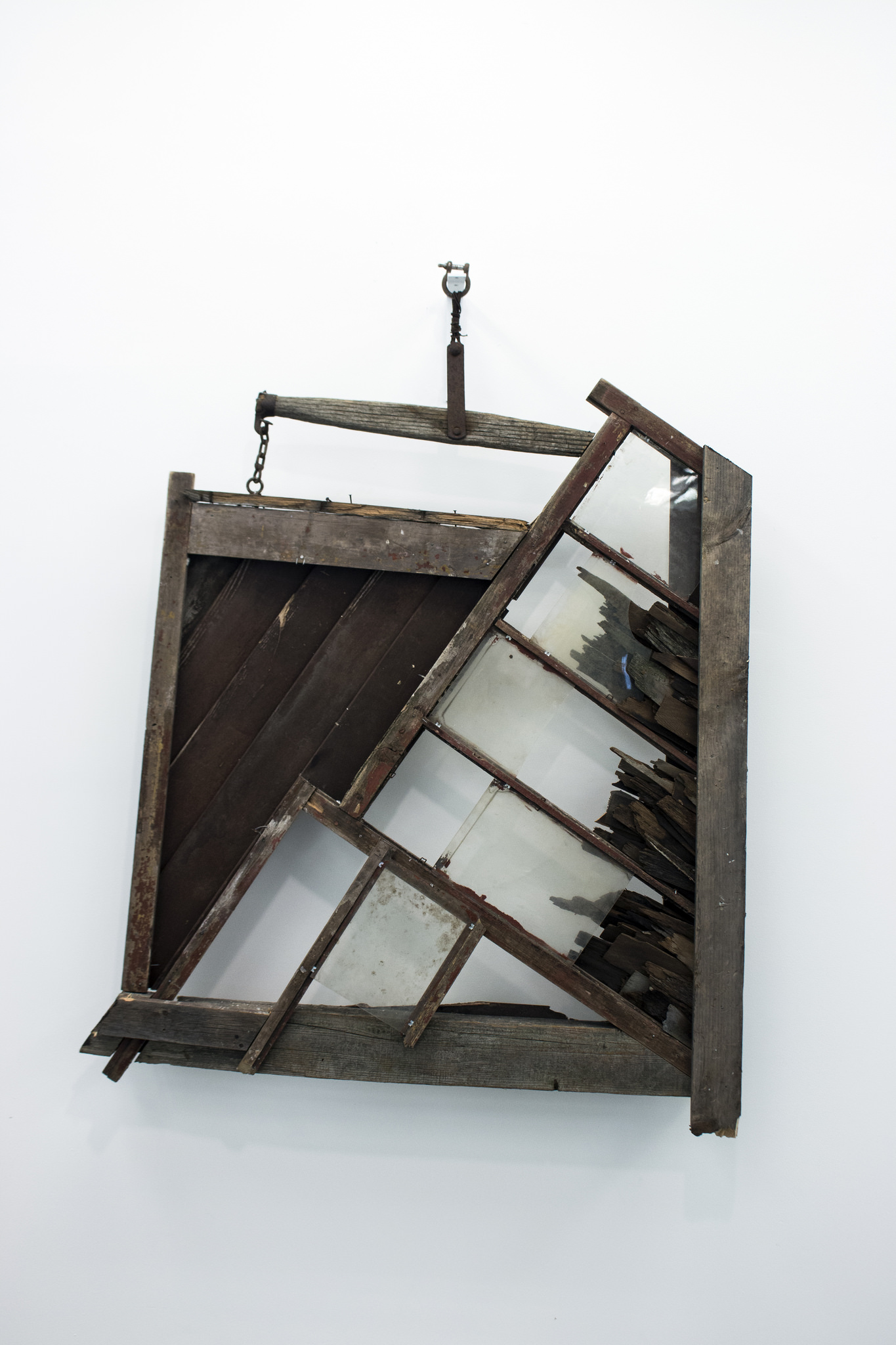  “Mended Pieces,” Benjamin Quesnel’s tobacco farm barn refuse assemblage, substantial and solid, yet precariously hung, at first seems wistful for a past Americana, but then turns cynical as we gaze through a window looking onto an opaque white wall.