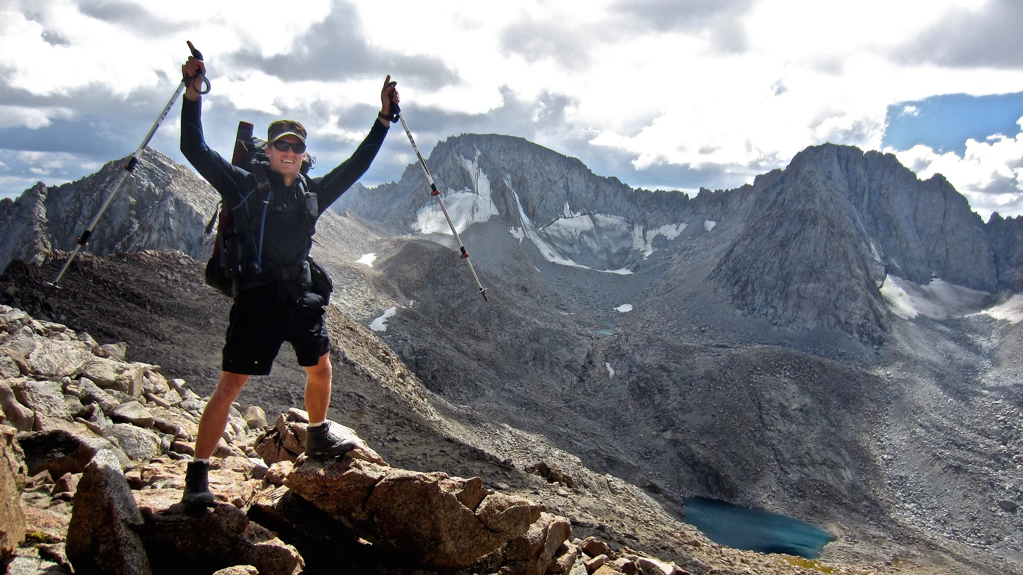 Hiker raises his arms in triumph above an alpine lake in Aspen Colorado