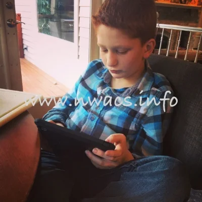 Nate sitting, holding and looking at his tablet/AAC device.