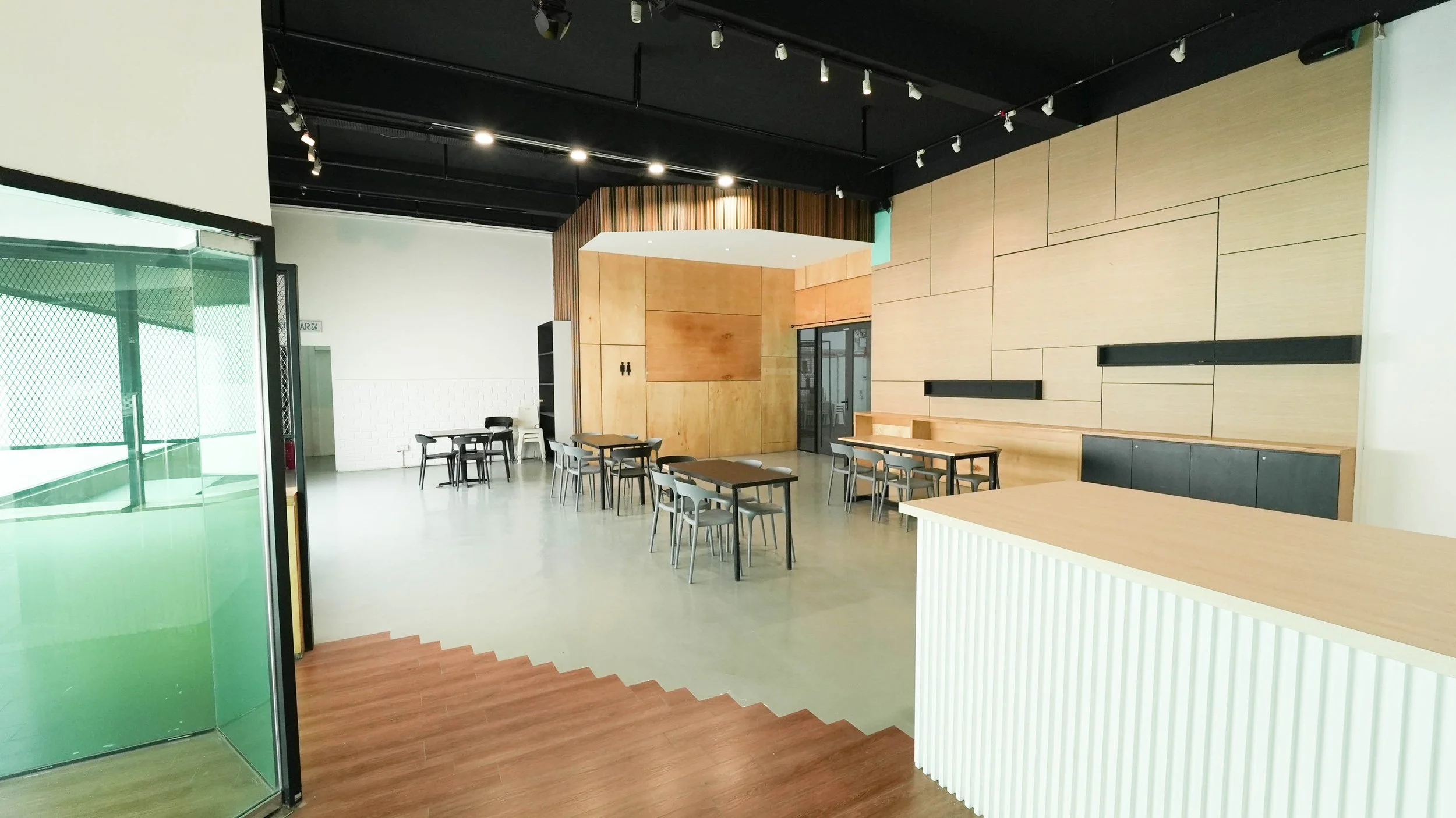 Empty modern cafe or restaurant with black tables and chairs, light wood wall panels, and a glass door on the left.