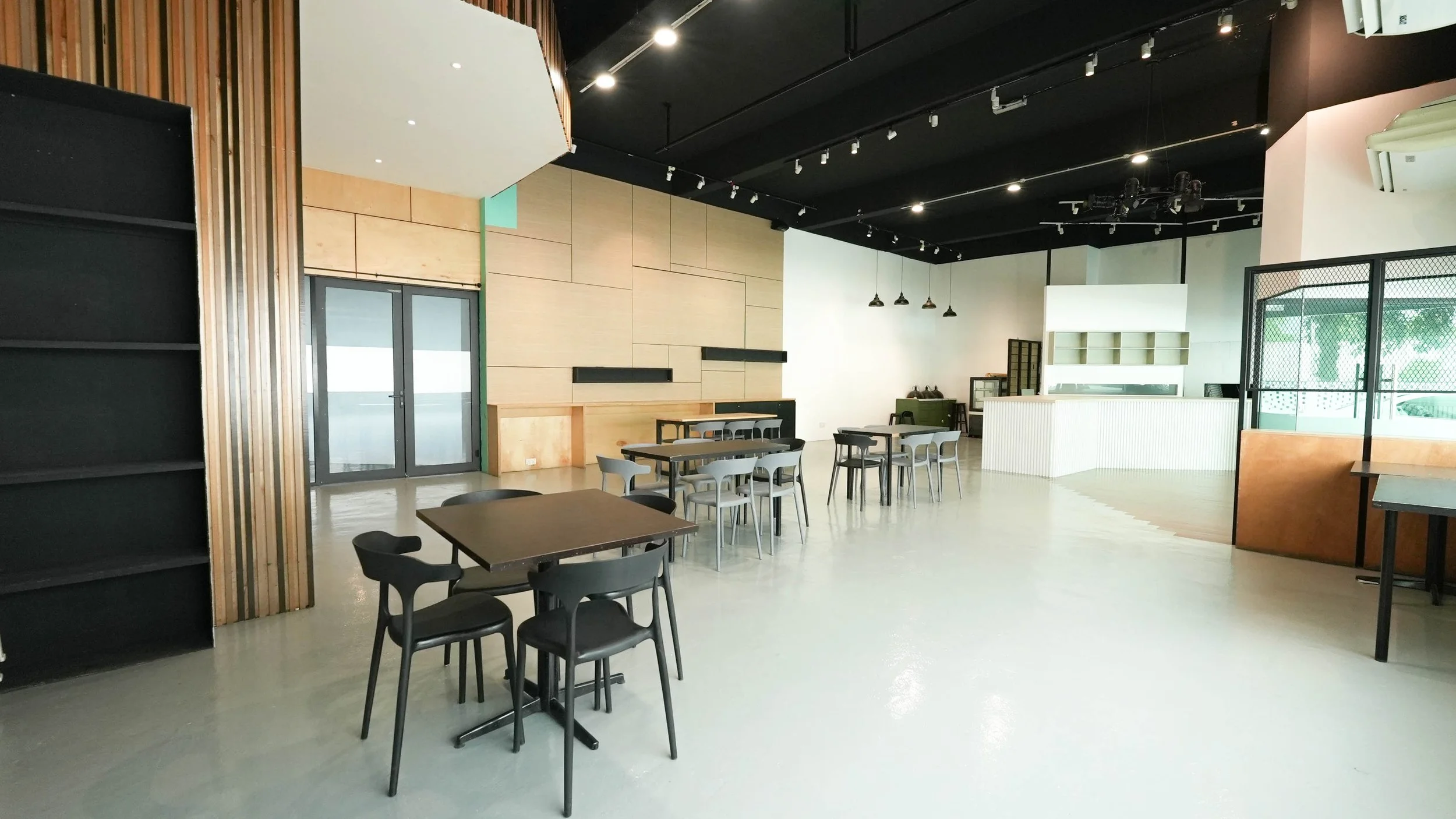 Empty modern cafe with black and gray tables and chairs, wooden wall accents, and large windows with green outdoor view.