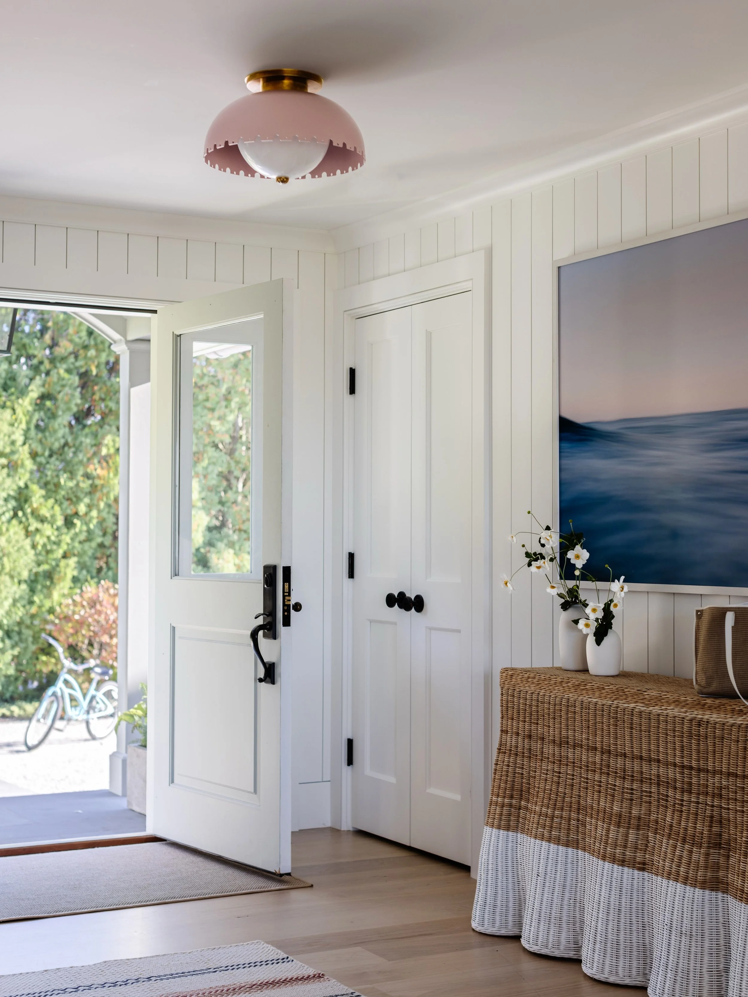 First impressions start at the front door, and this entryway perfectly sets a relaxed, coastal tone the moment you step inside. 🌊  Clean white vertical paneling creates a bright backdrop, beautifully contrasting the wicker console&rsquo;s warm, sand