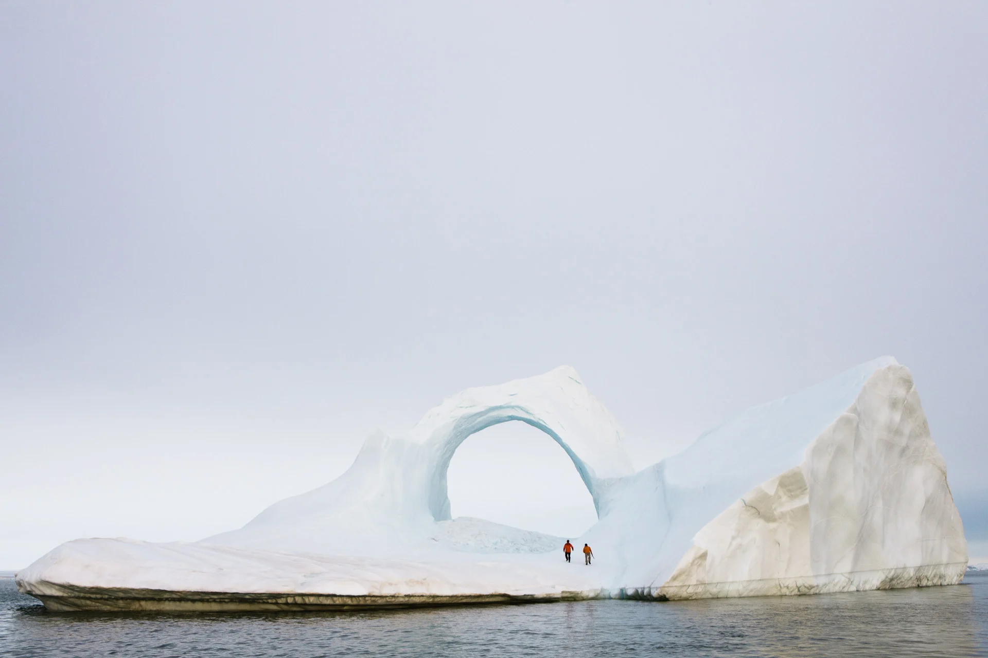 Two scientists walk under an arch in an iceberg