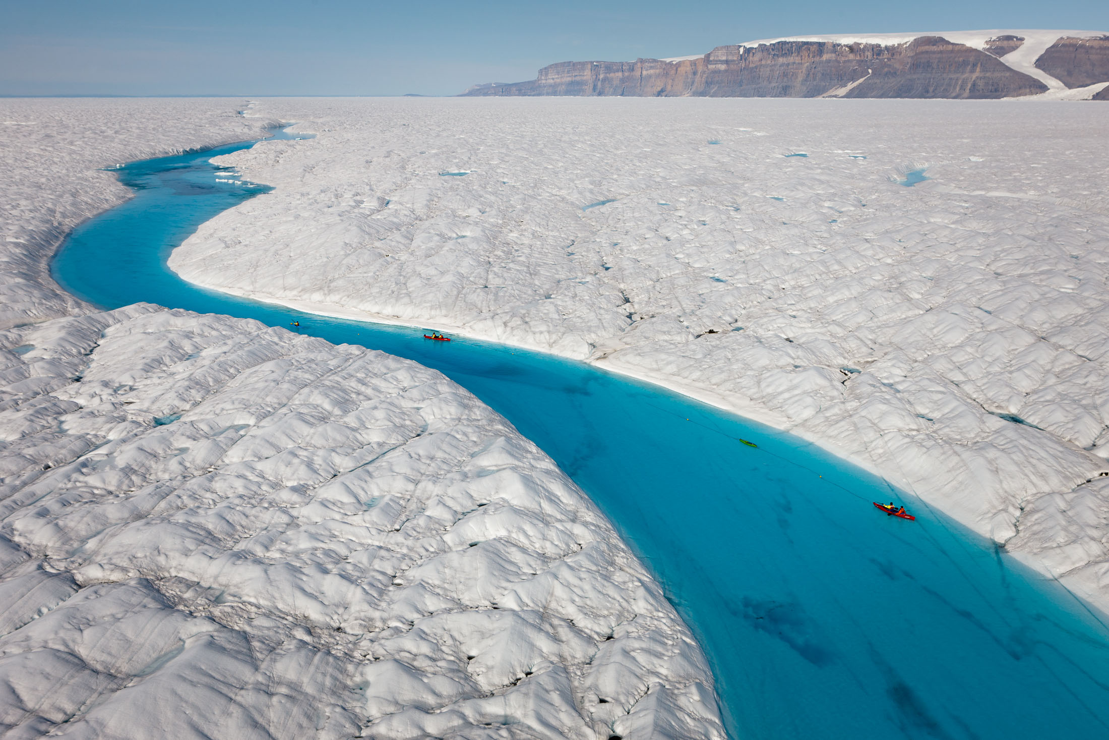 A vivid blue meltwater ravine running through the surface of Petermann Glacier on Greenland