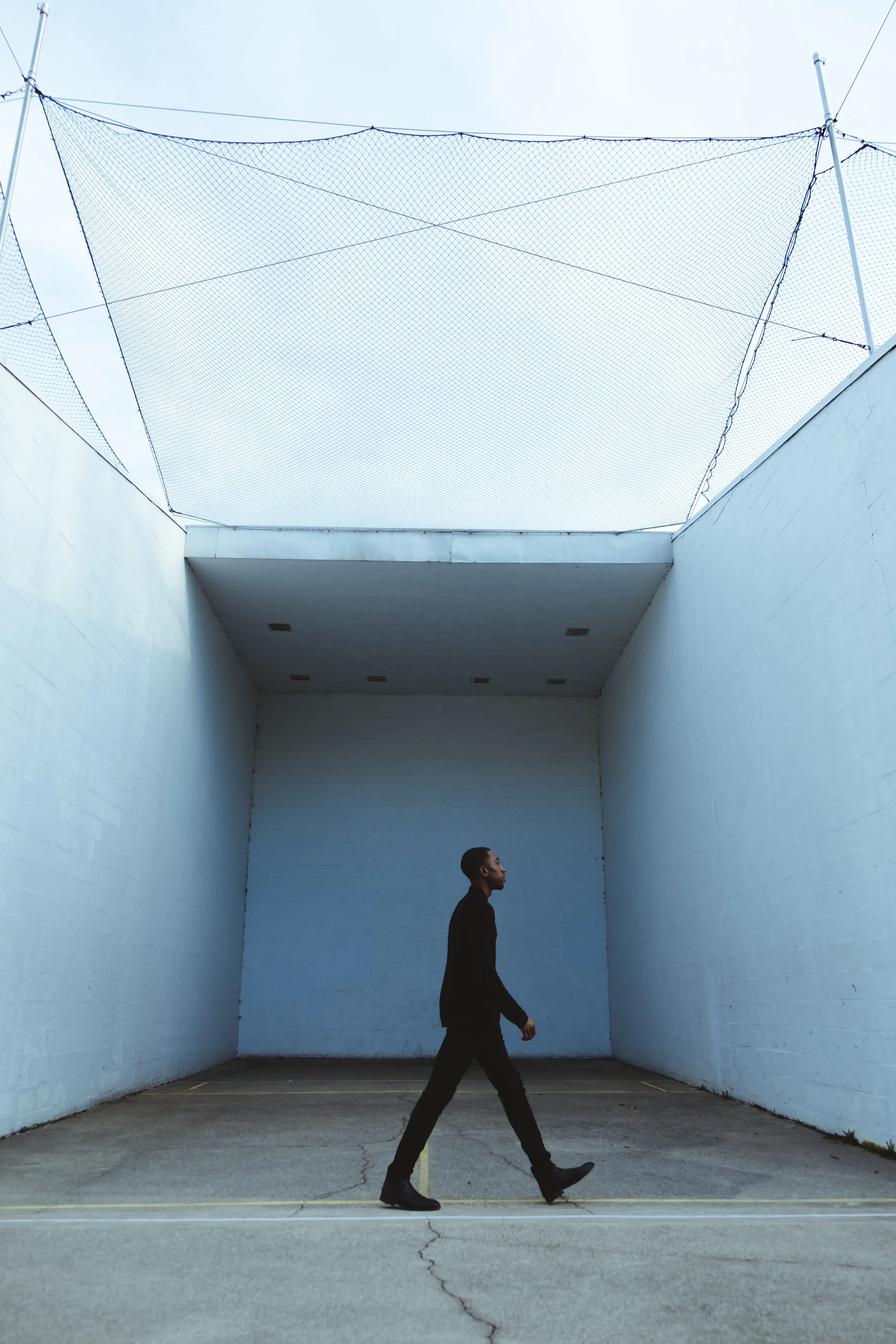 A man walking in an open, walled, concrete area with high walls and a sky roof with netting overhead.