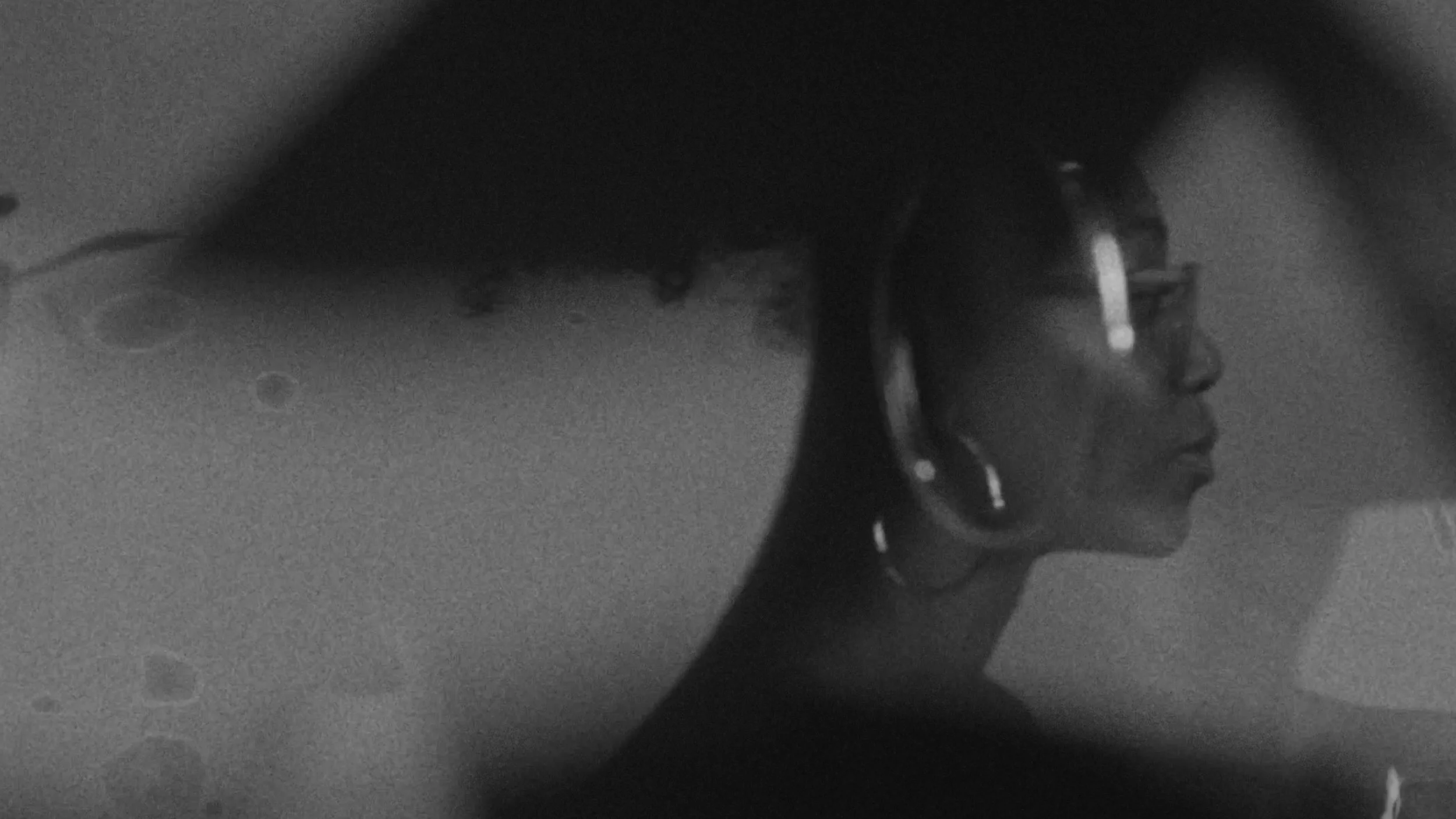 A profile of a woman wearing glasses, with curly hair, seen through the window of a vehicle at night.