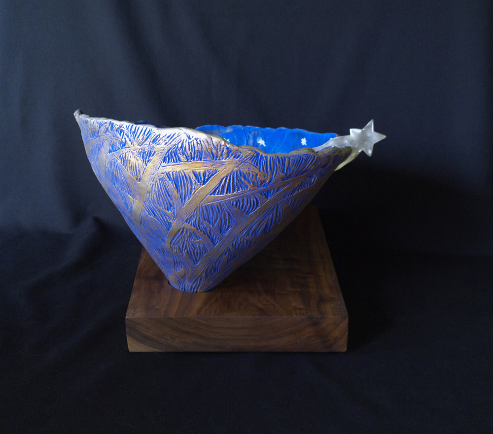 Comets and Silver Shooting Star Bowl I bathe under the stars each night. A dark tree line rings my farm. I imagine the stars and comets breaking through the night sky. This porcelain bowl was hand built and hand carved from slab porcelain clay. It was painted with mason stains, underglaze and gilded. It was bisqued and fired to cone 6. The walnut base was finished, hand oiled and rubbed. The walnut base was then routed into to fit the bowl’s base. The bowl was secured into it. Then the feet were attached to it. The Argentium silver shooting star was hand cut and finished - then mounted through the bowl. Size:12 inches h x 14 inches w x 17 inches d